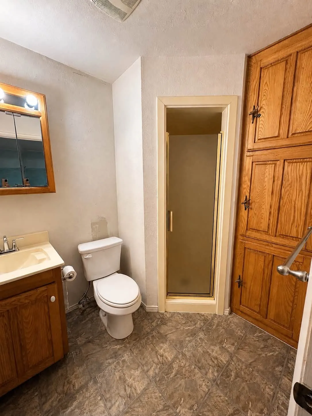 Bathroom featuring a wood-finish vanity with an integrated sink, a white toilet, and a stand-up shower with a frosted glass door