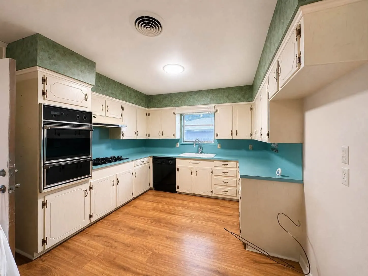 Kitchen featuring extensive cream cabinetry with gold-toned hardware, a double wall oven, and a gas cooktop