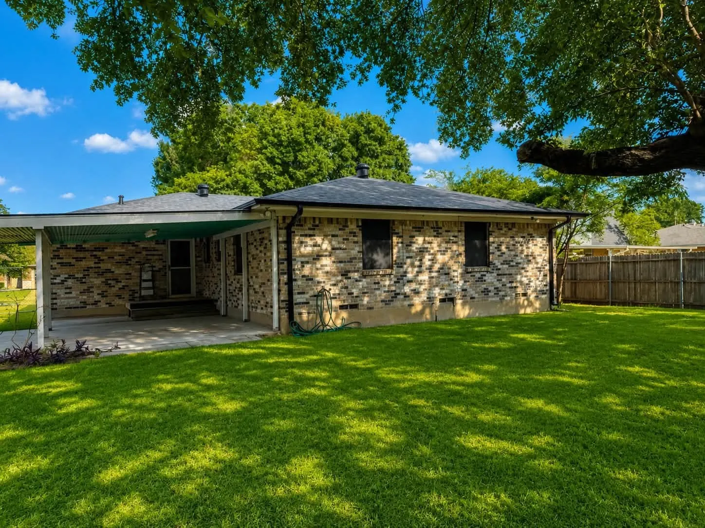 Expansive backyard featuring a lush lawn, a covered patio, and mature trees