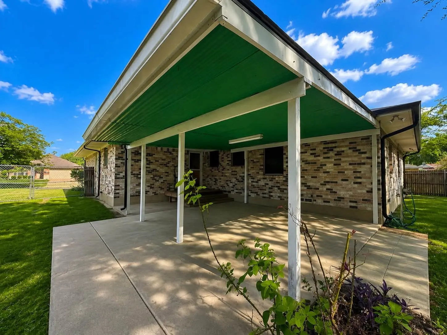 Rear exterior featuring a covered patio with a green soffit, brick facade, concrete patio surface, and a manicured lawn