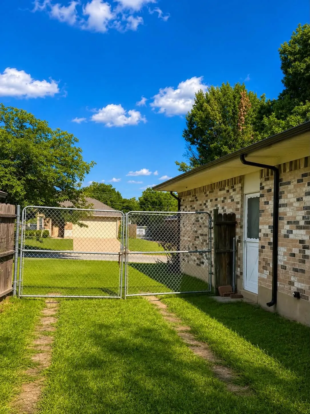 Brick exterior featuring a white entry door, chain-link gate, and a grass pathway