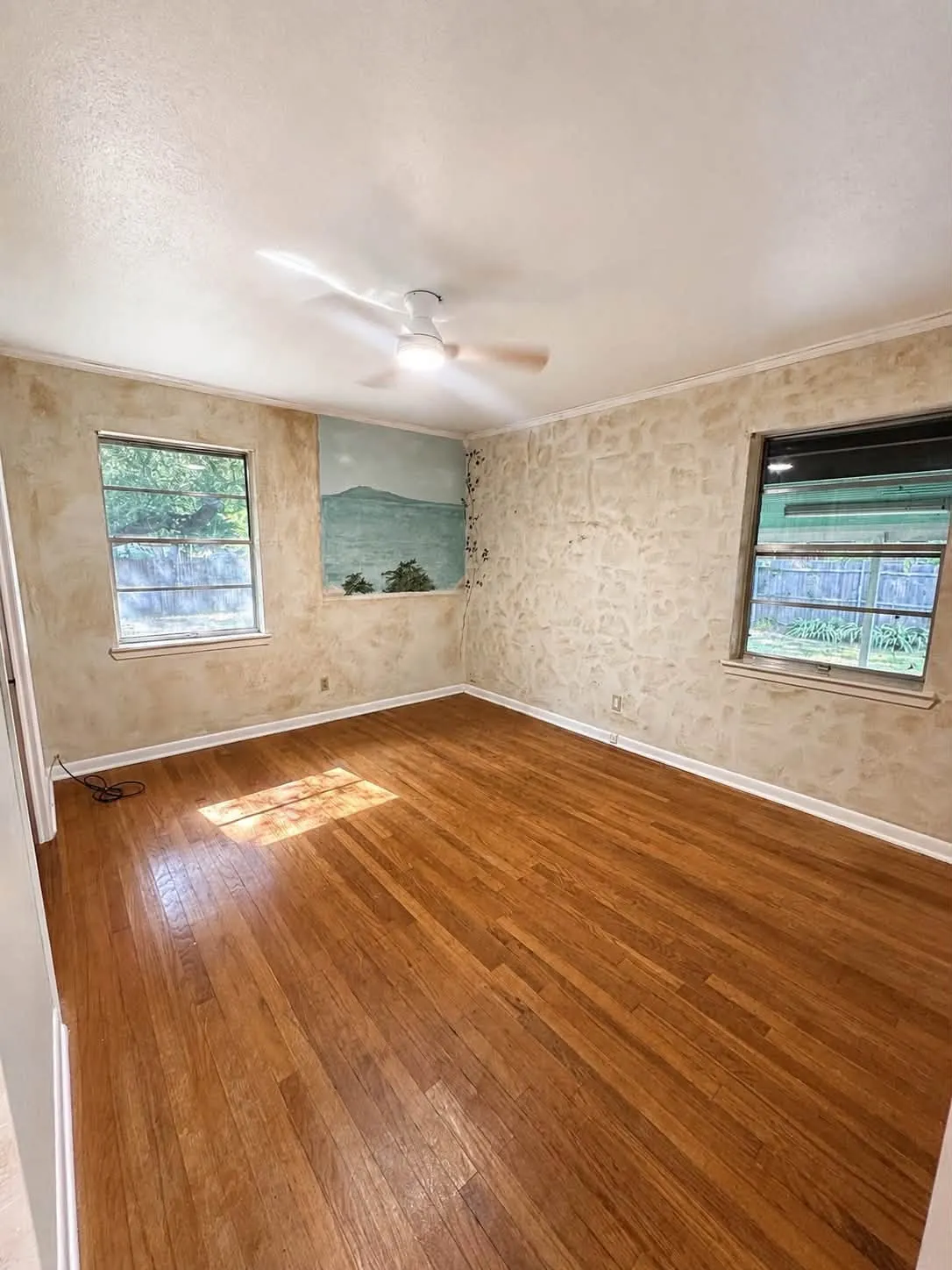Hardwood flooring throughout, complemented by two windows and a ceiling fan with integrated lighting