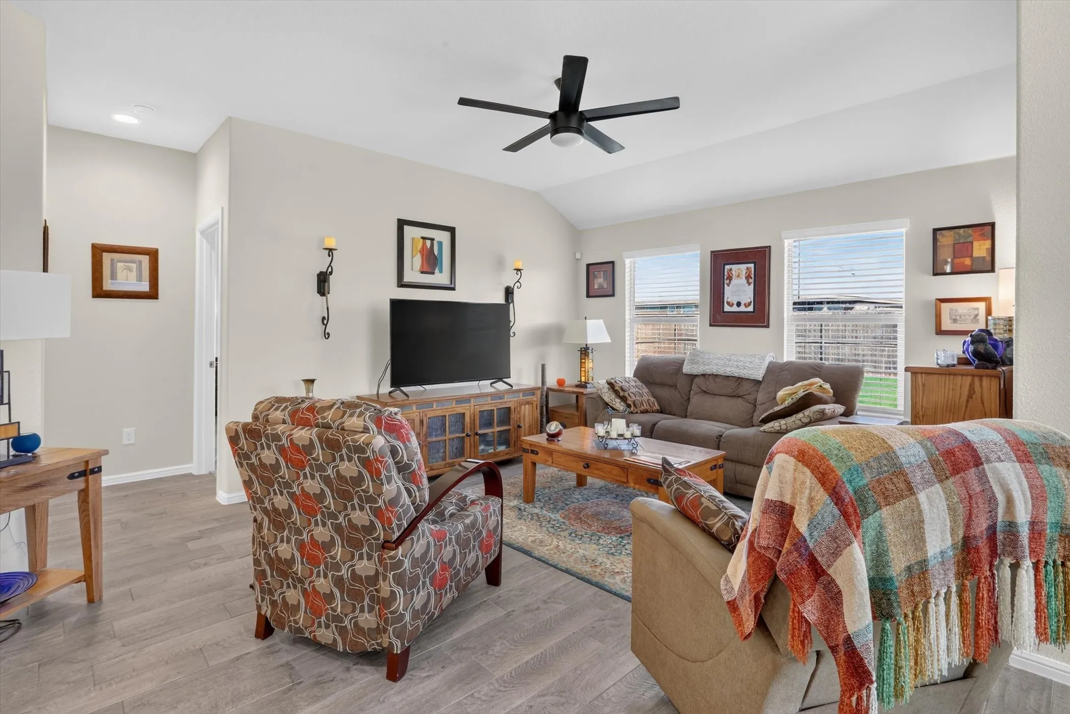 Spacious living area featuring wood-finish flooring, vaulted ceiling, and a ceiling fan