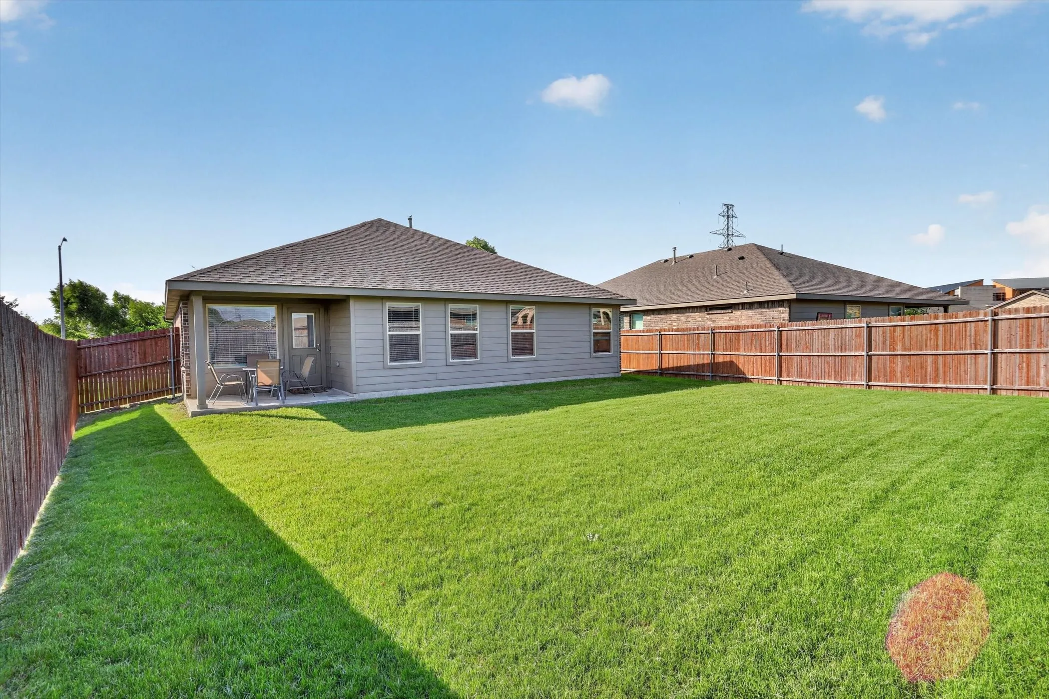 Expansive green lawn with a screened patio, privacy fencing, and a neutral-toned exterior