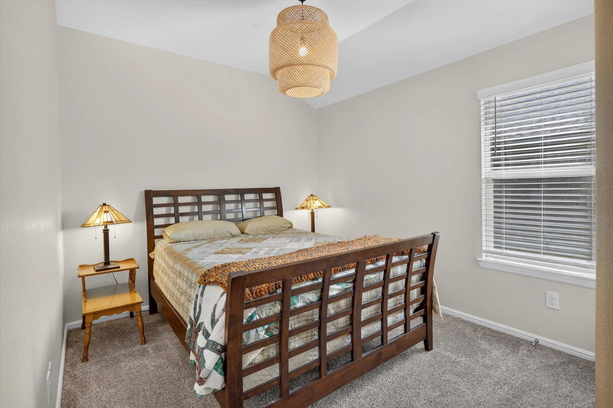 Carpeted room featuring a window with blinds, a vaulted ceiling, and a woven pendant light fixture