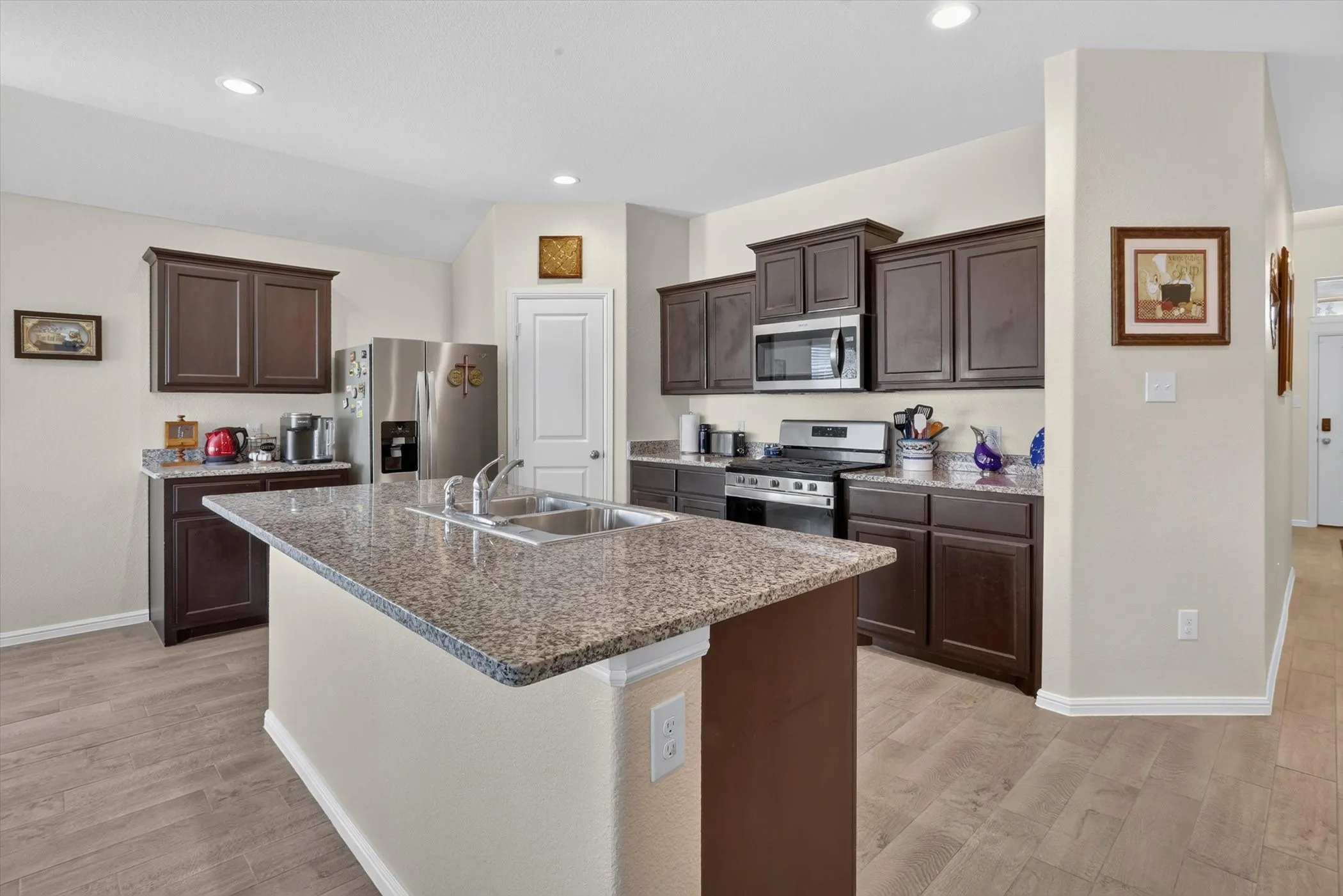 Kitchen featuring an island with a double basin sink, dark wood cabinetry, stainless steel appliances, speckled countertops, and wood-finish flooring