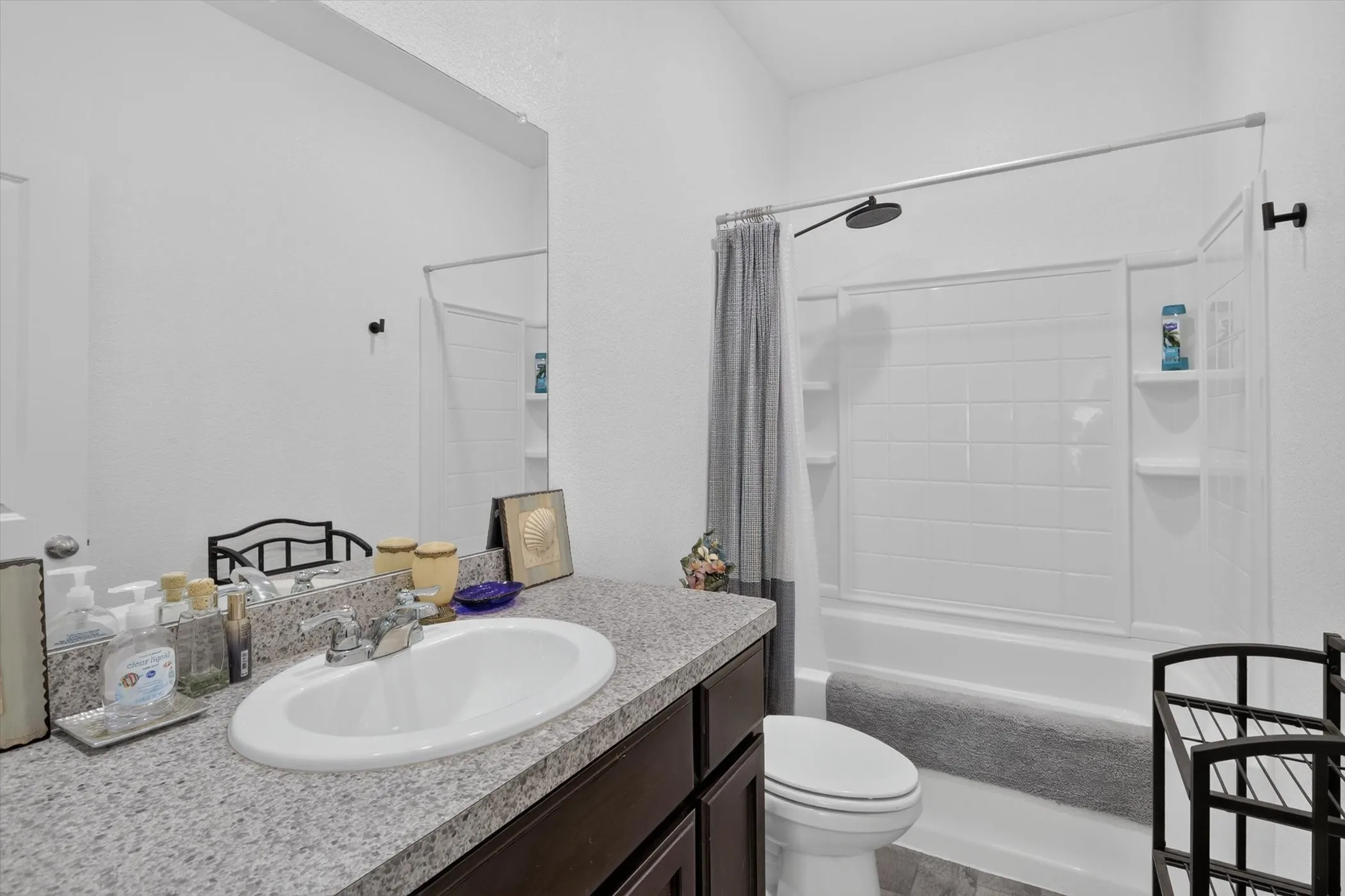 Bathroom featuring a dark wood-finish vanity with a speckled countertop, an integrated sink, and a large mirror