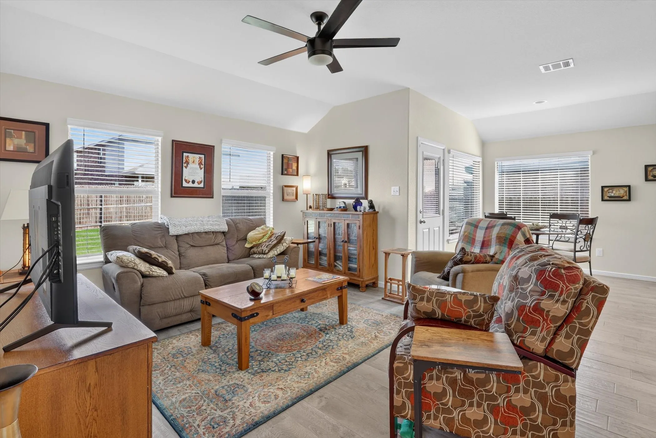 Spacious living area featuring vaulted ceilings, wood-finish flooring, ample natural light from multiple windows, and a ceiling fan