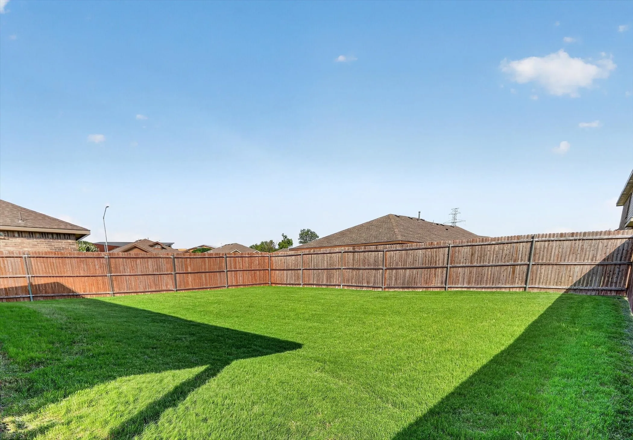 Expansive backyard featuring a lush lawn, perimeter wood fencing, and a clear sky overhead
