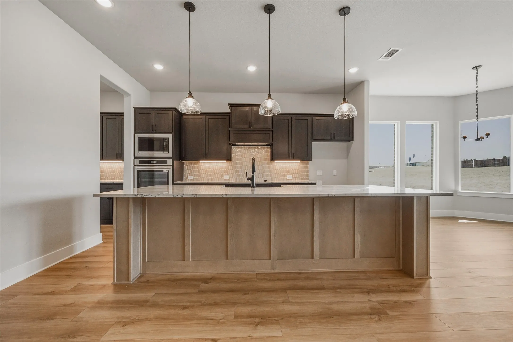 Kitchen island with a light wood-tone finish, pendant lighting, built-in double oven, and wood-finish flooring