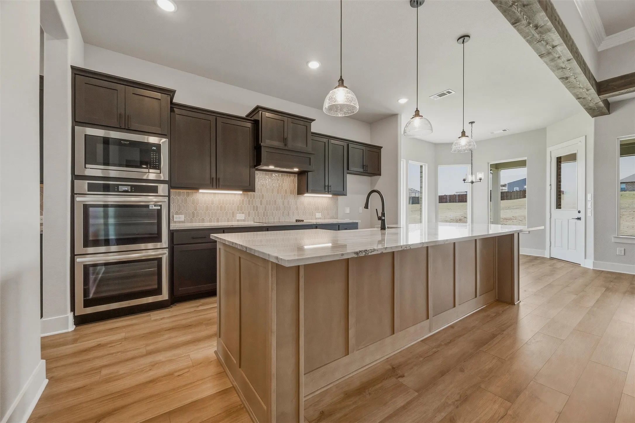 Kitchen featuring a large island with countertop, stainless steel double ovens, dark wood-finish cabinetry, wood-finish flooring, and pendant lighting