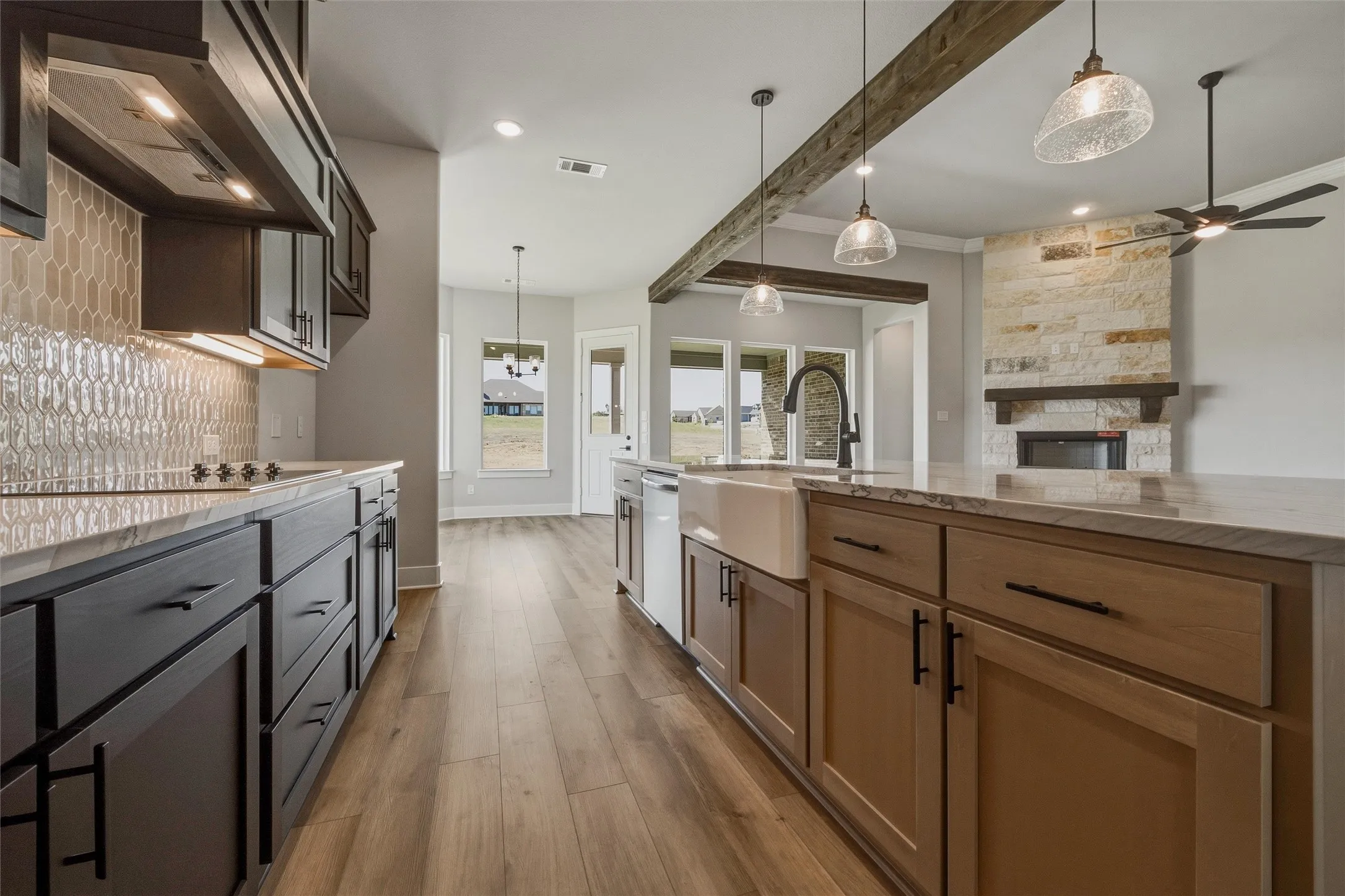 Kitchen featuring wood-finish flooring, two-tone cabinetry, a farmhouse sink, and a stone fireplace with a wood mantel