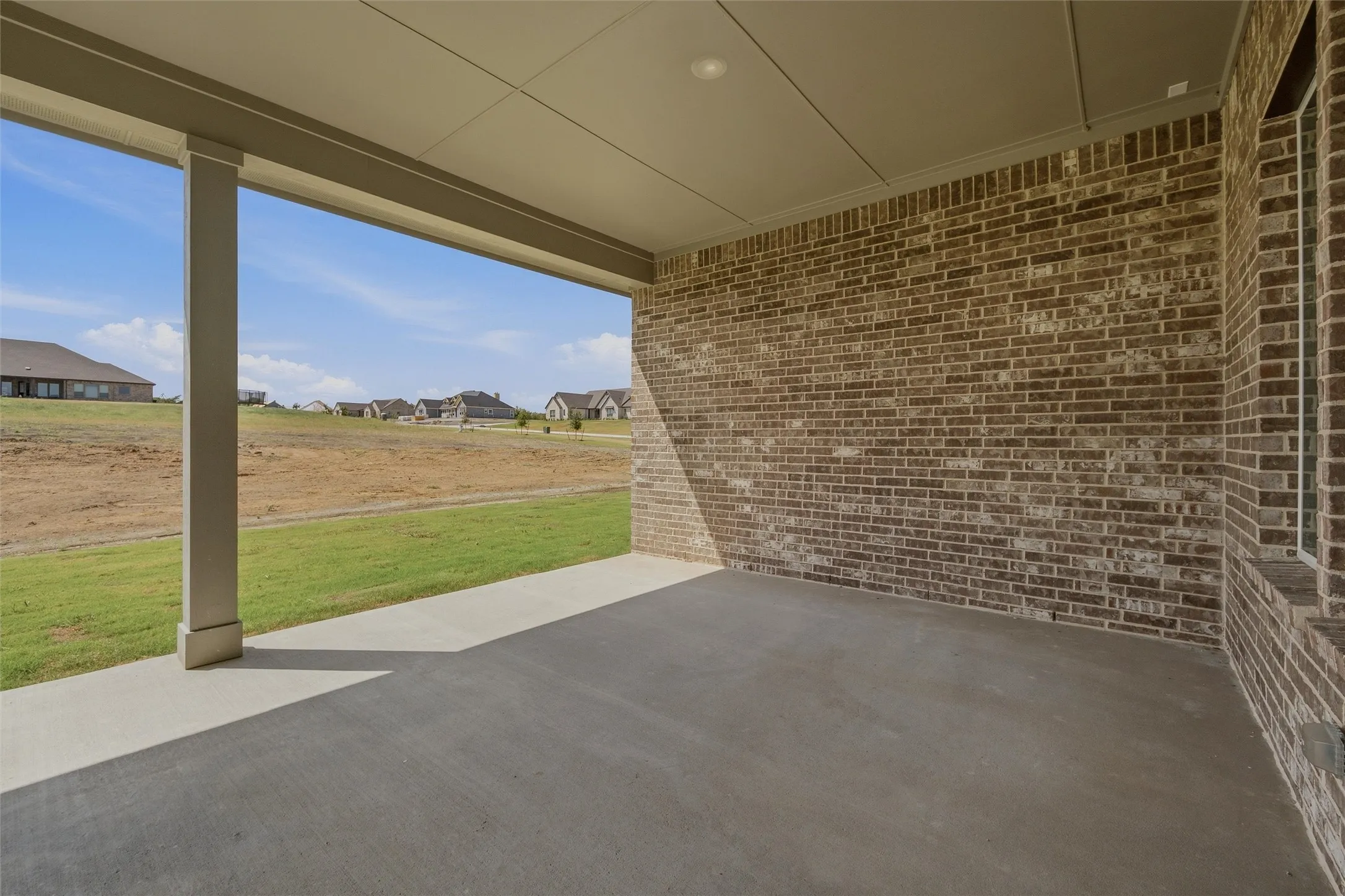 Expansive covered patio with concrete flooring, brick exterior wall, and recessed lighting