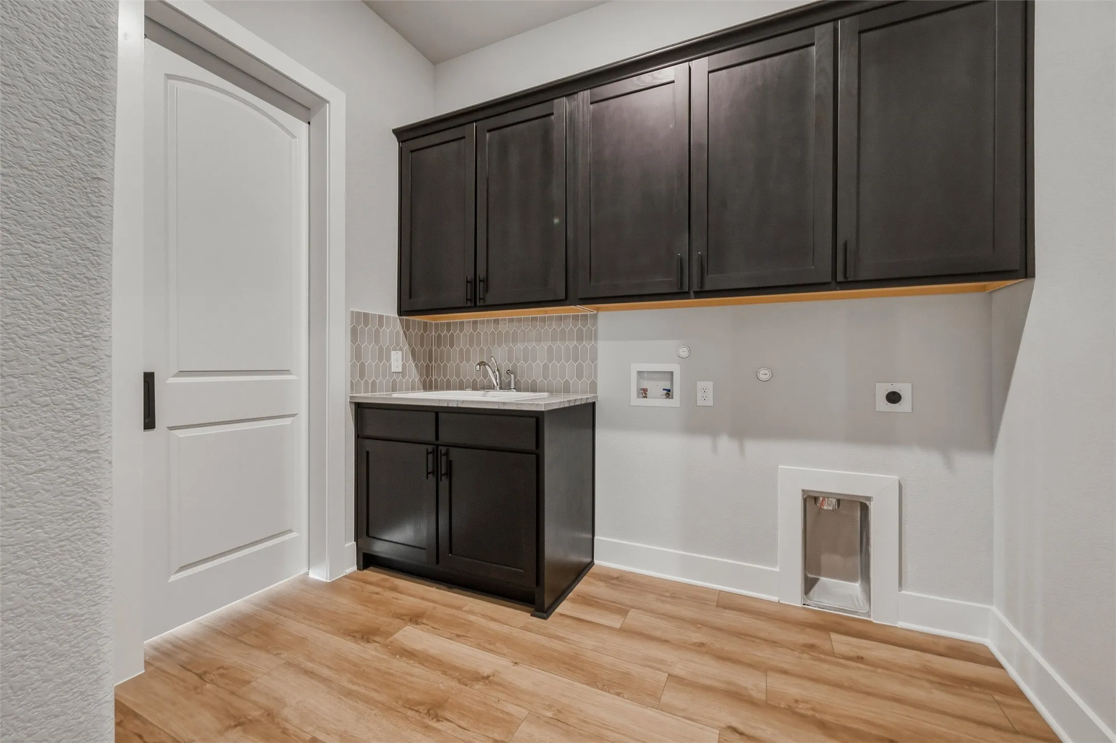 Wood-finish flooring, dark wood cabinetry, white countertop, integrated sink, and gray geometric tile backsplash