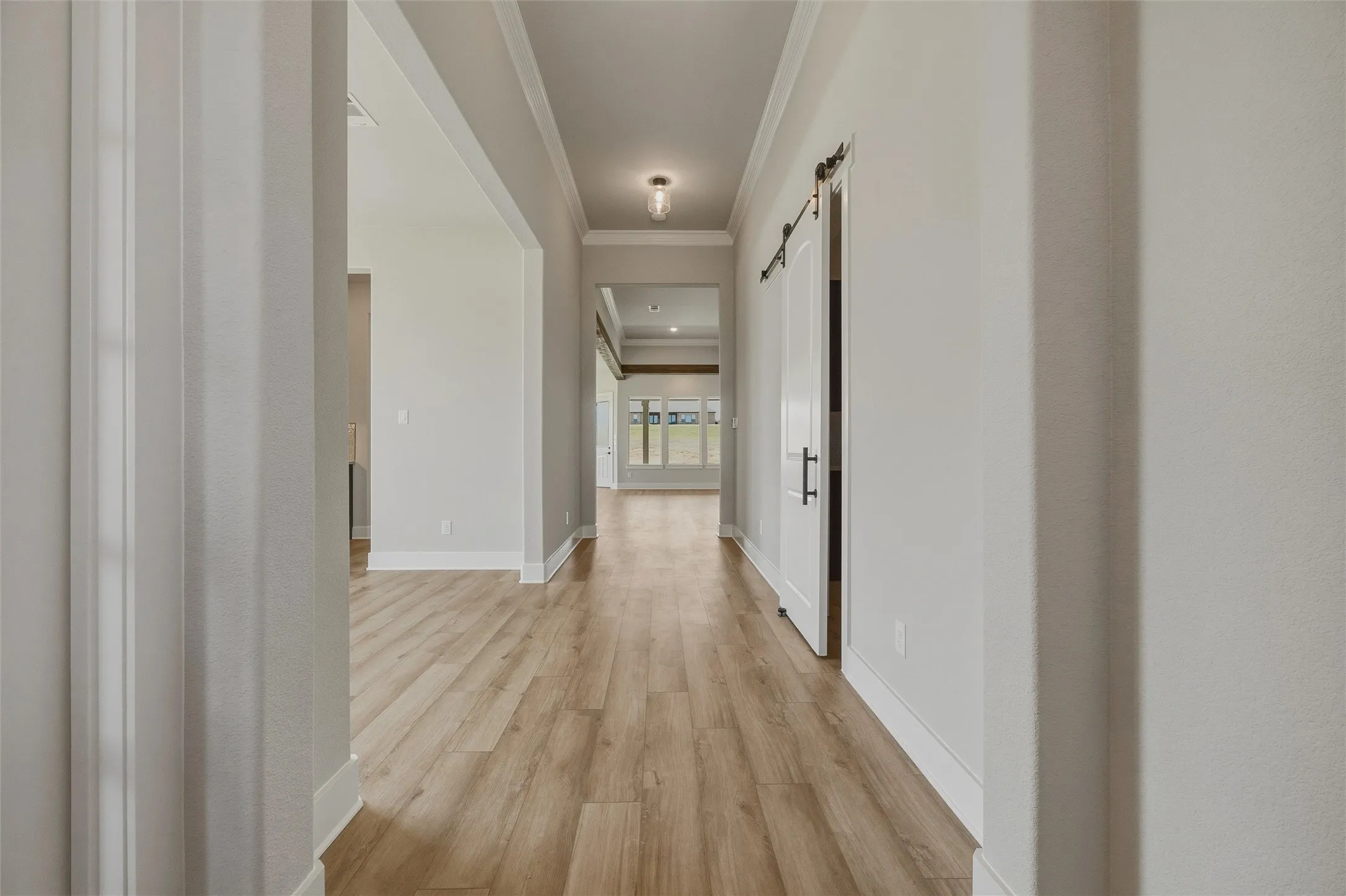 Hallway featuring wood-finish flooring, a barn door with black hardware, recessed lighting, and crown molding