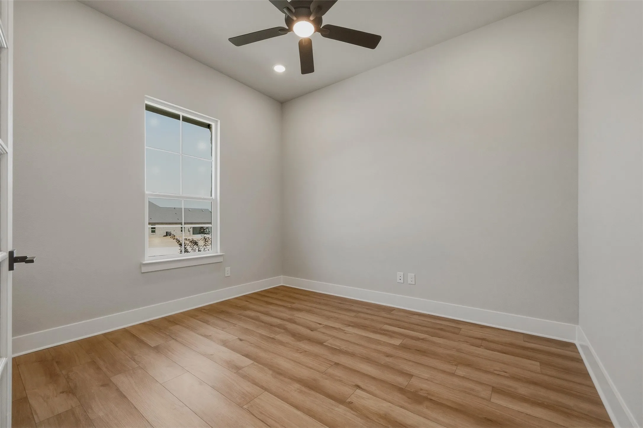 Neutral wall color, wood-finish flooring, white trim, ceiling fan with integrated lighting, and a double-pane window