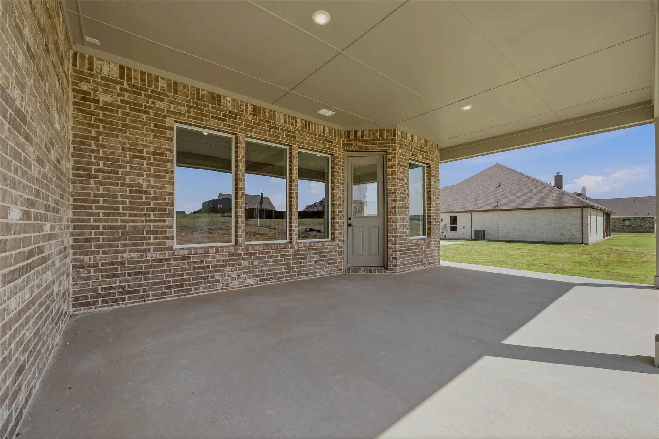 Covered concrete patio with recessed lighting, brick exterior, and multiple windows