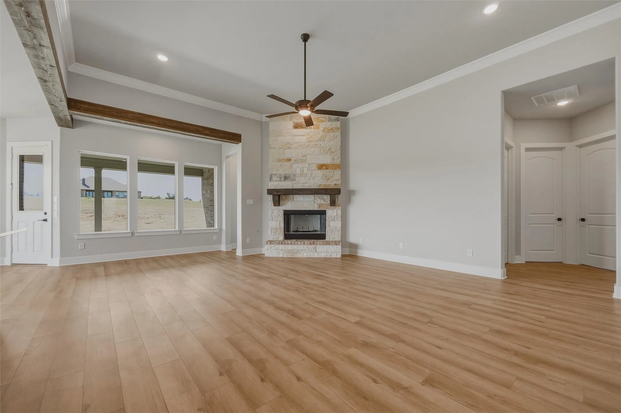 Vaulted ceiling with exposed wood beams, stone fireplace with a wood mantel, light wood-finish flooring, recessed lighting, and multiple windows