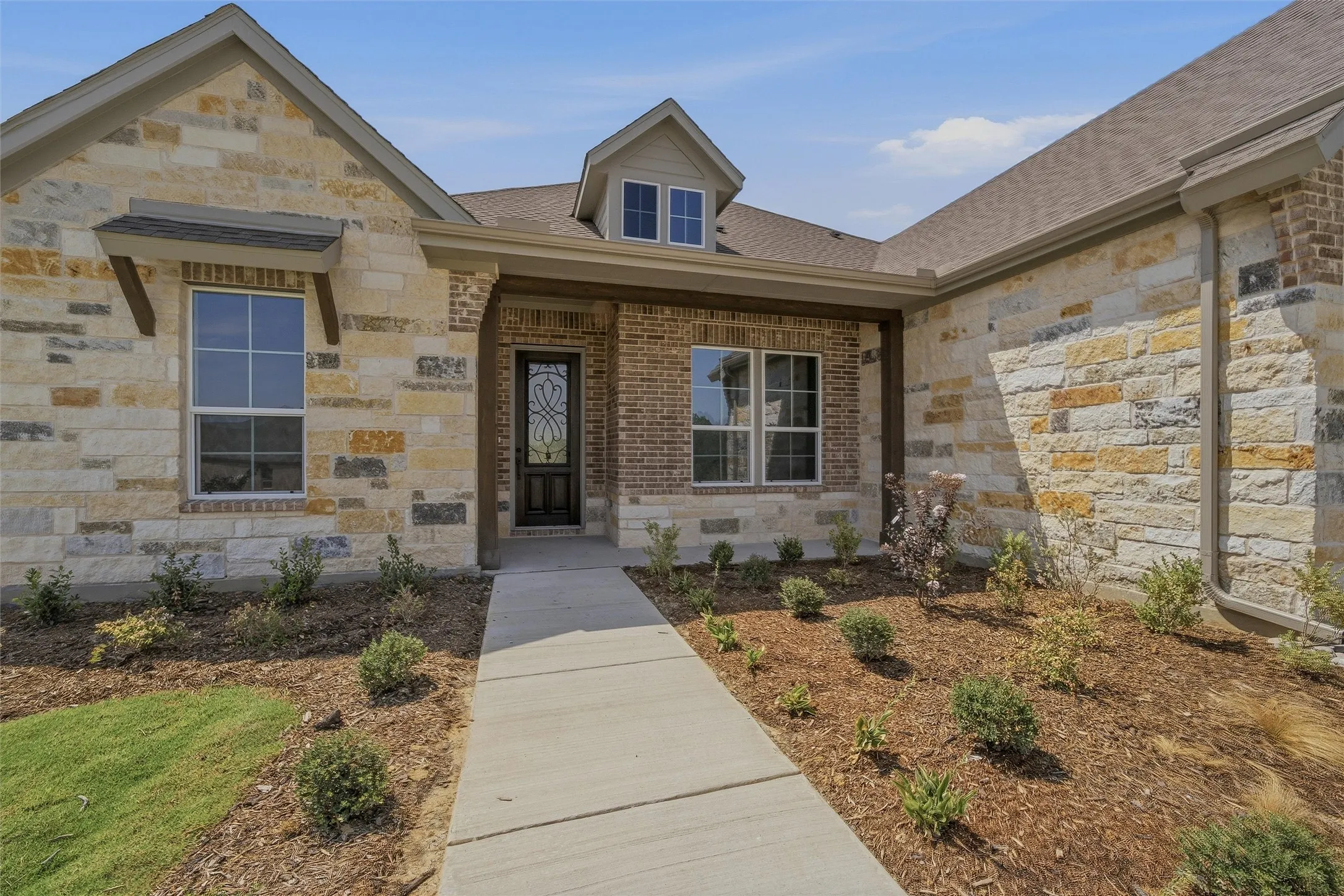 Stone and brick veneer exterior with a concrete walkway, decorative front door, and a dormer window