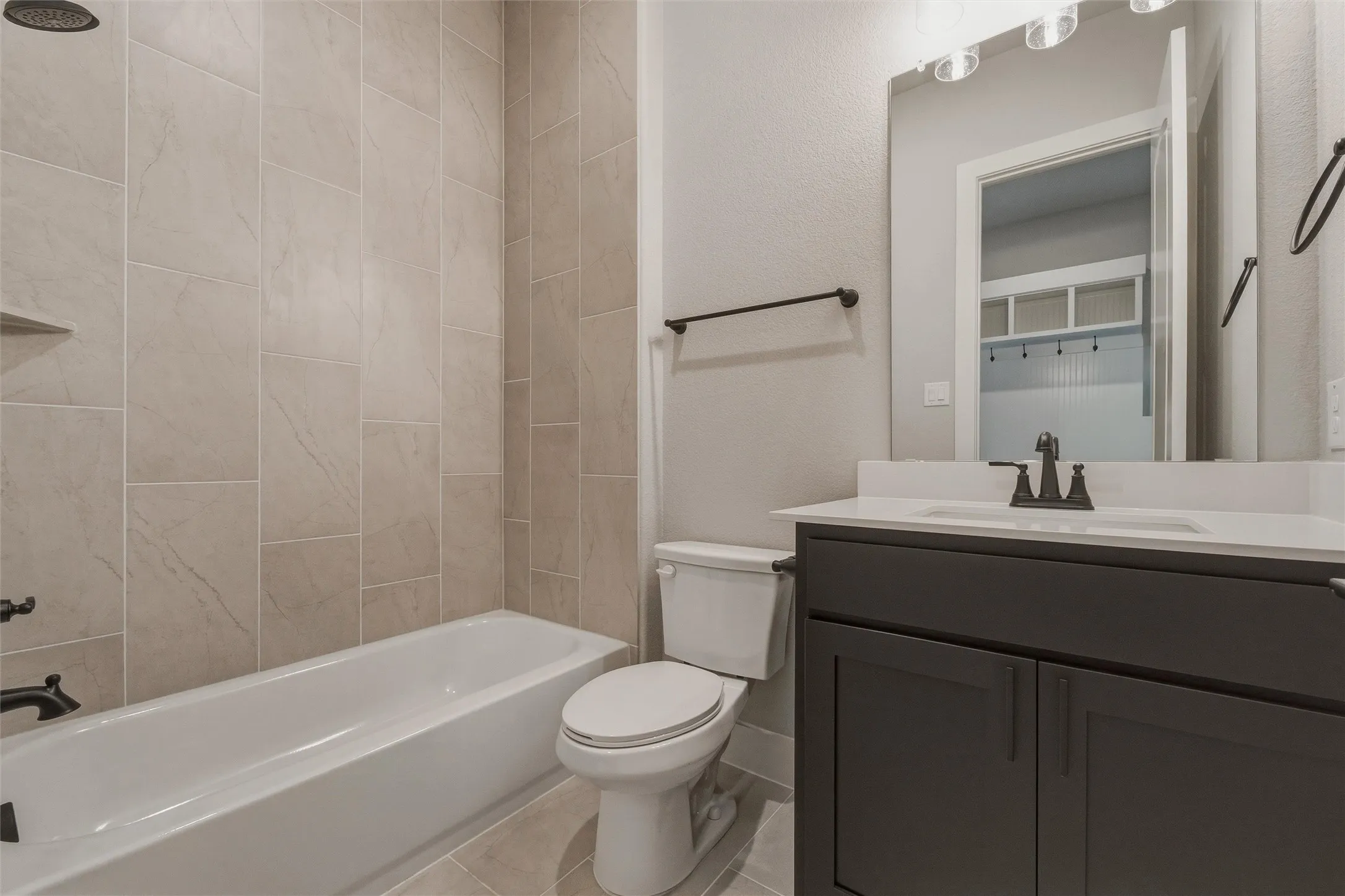 Full-size bathtub with tiled surround, dark wood-finish vanity with countertop, rectangular undermount sink, and matte black fixtures
