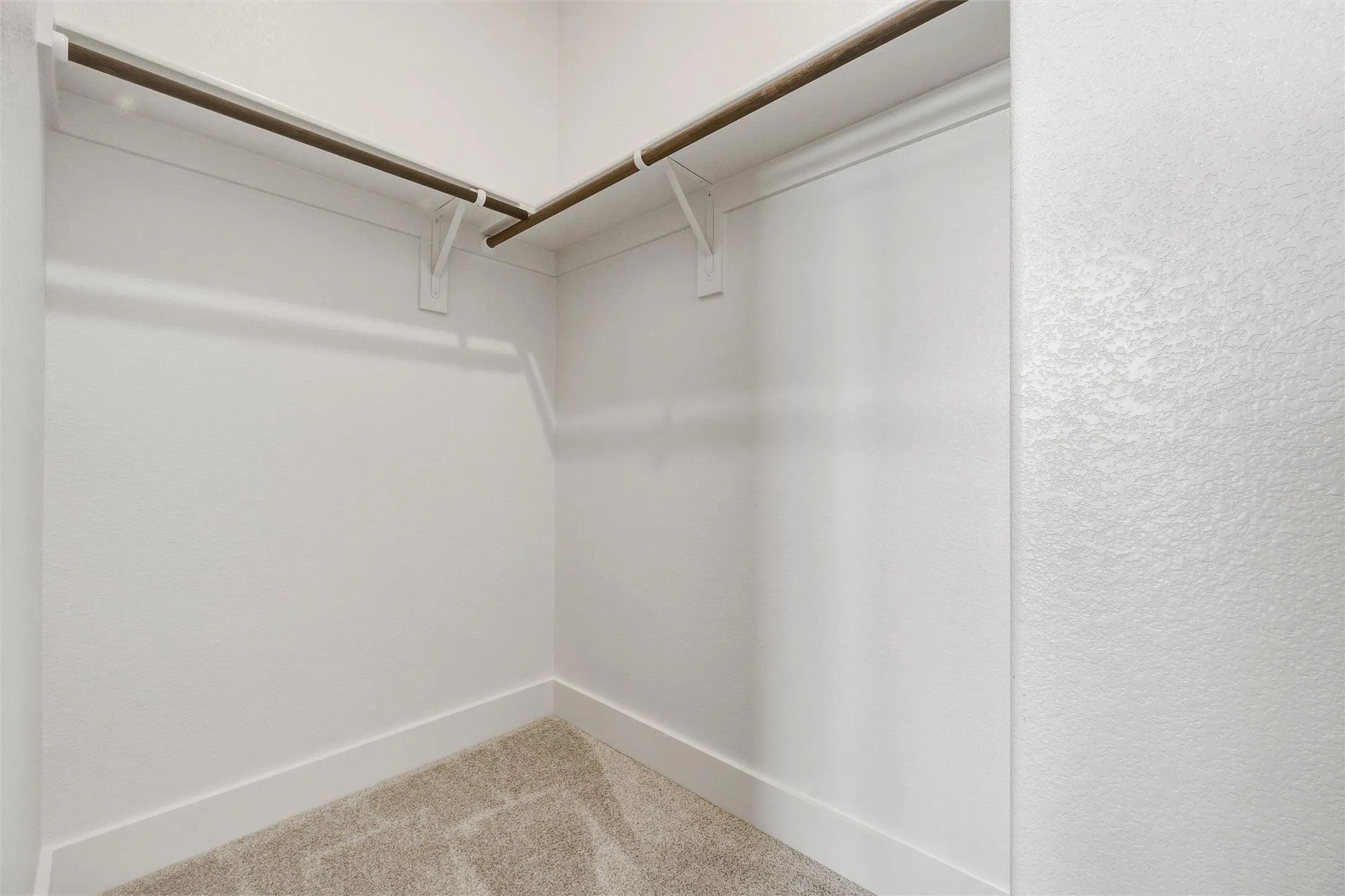 Recessed closet with light-colored carpeting, white walls, and built-in shelving with hanging rods