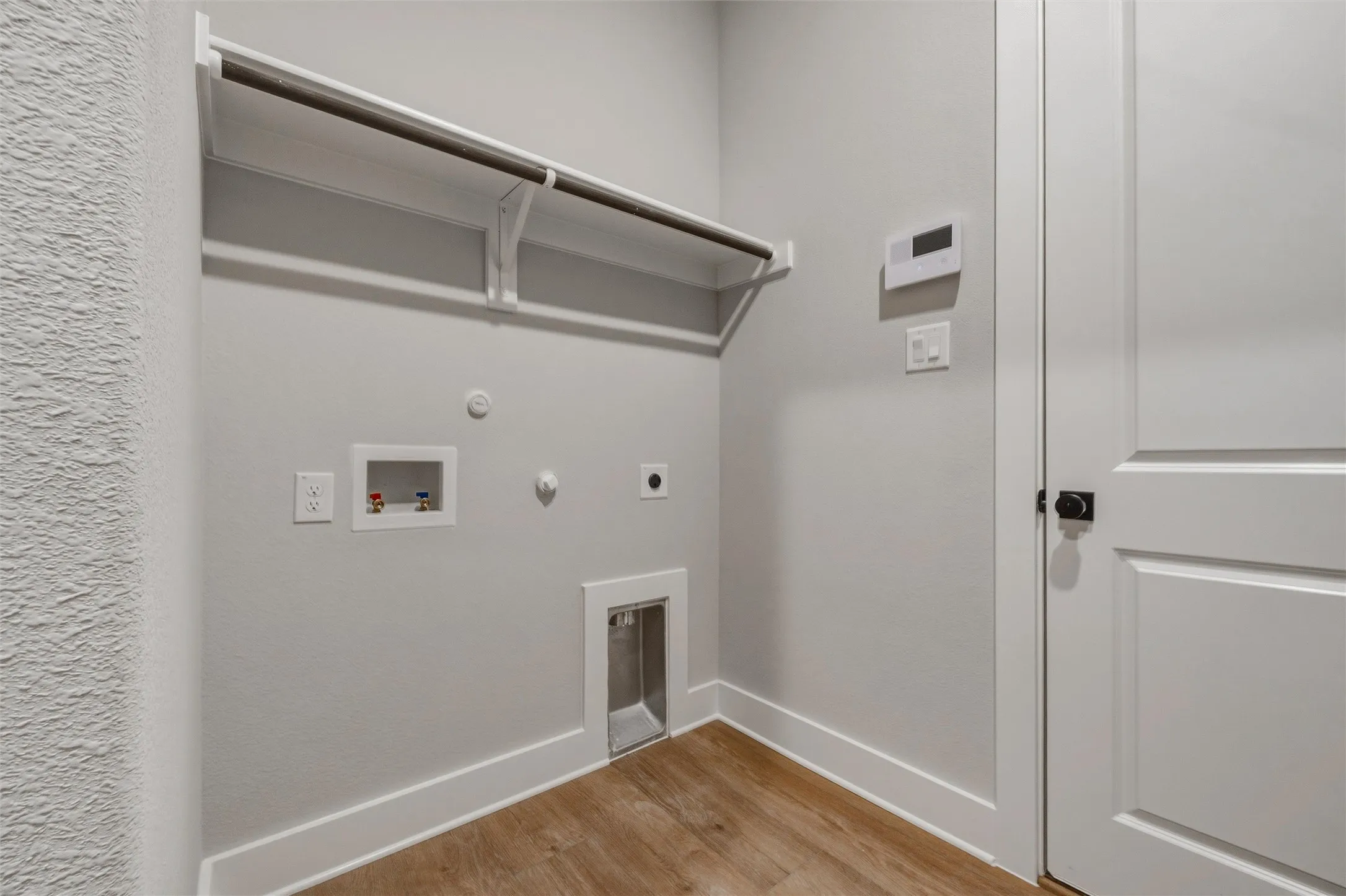 Laundry area featuring wood-finish flooring, a built-in hanging rod, dedicated utility connections, and a paneled door with matte black hardware