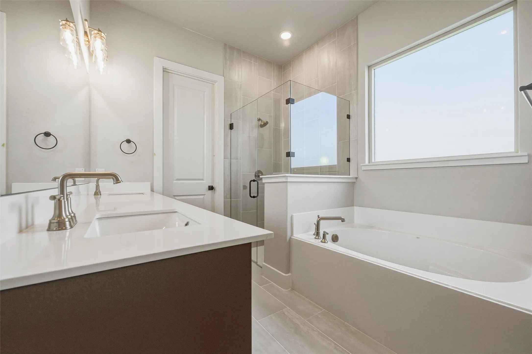 Dual vanity with white undermount sinks, a freestanding soaking tub, and a glass-enclosed shower with tile surround
