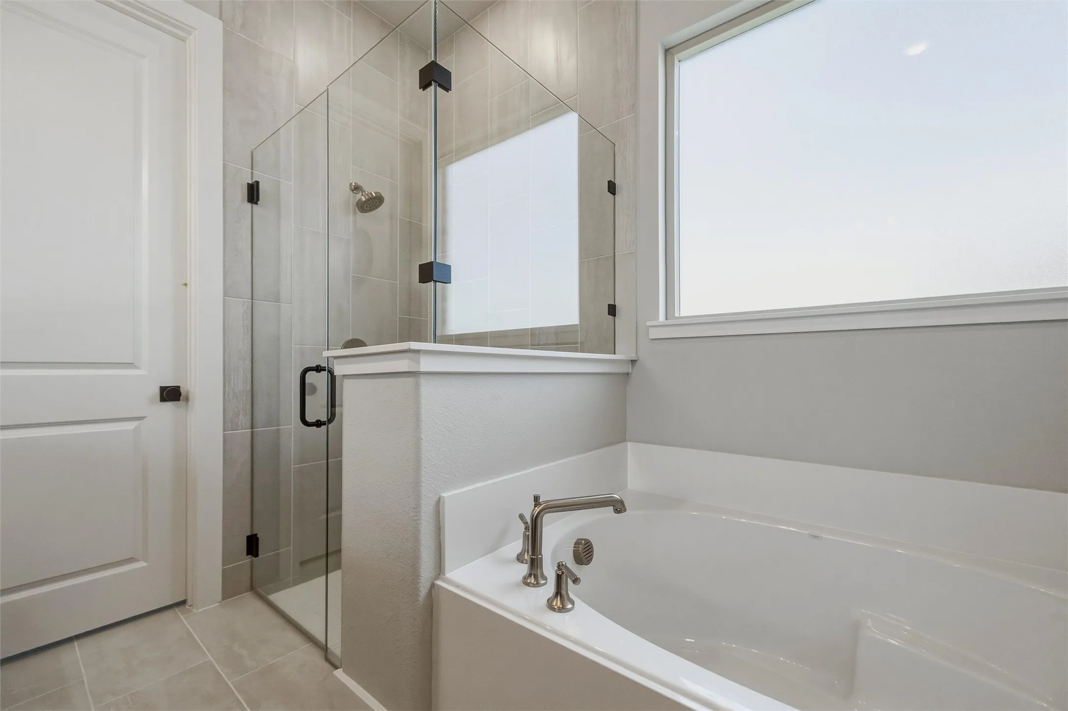 Spacious bathroom featuring a glass-enclosed shower, built-in soaking tub, and large privacy window