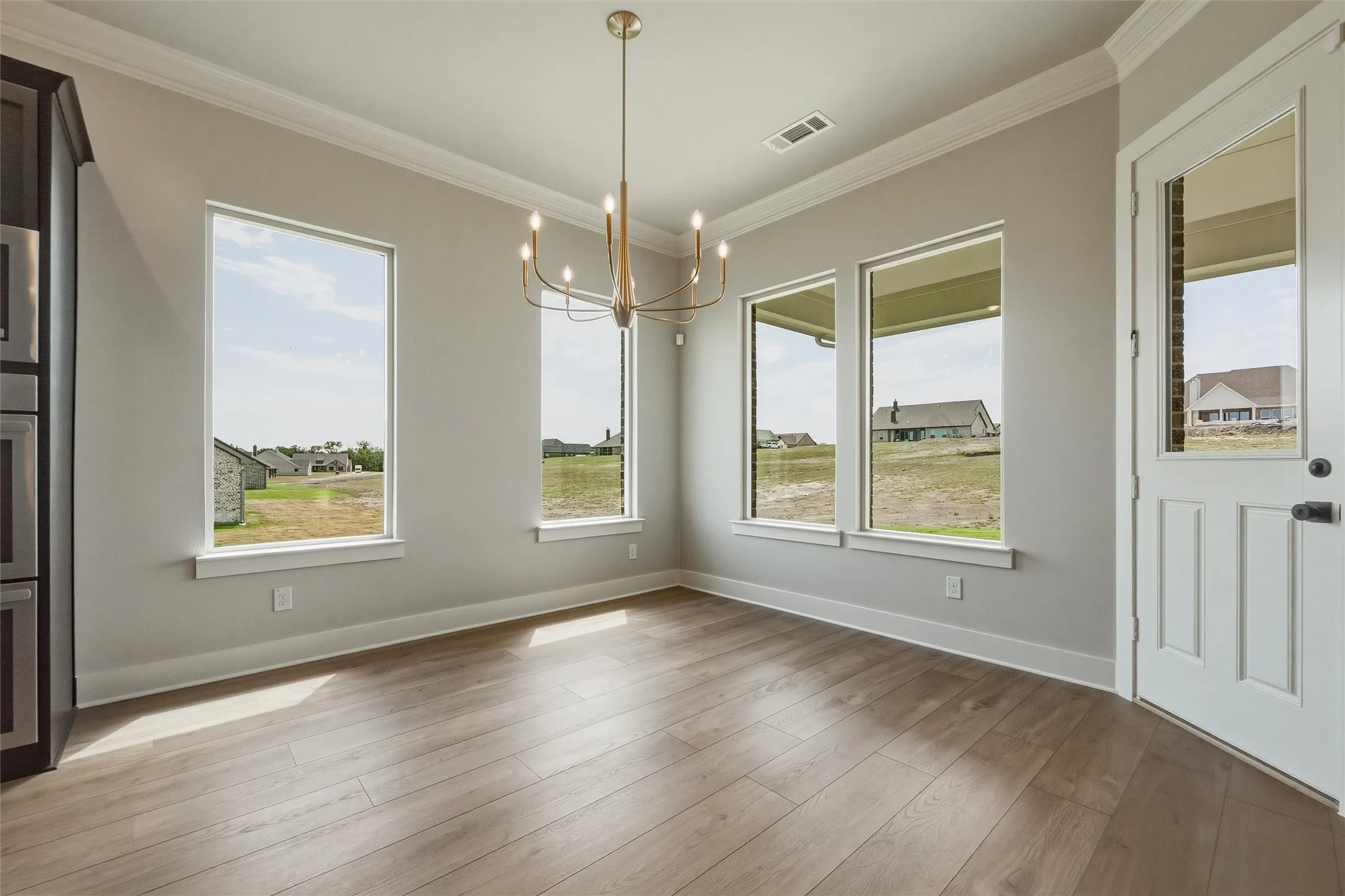 Wood-finish flooring, multiple tall windows, crown molding, and a modern chandelier