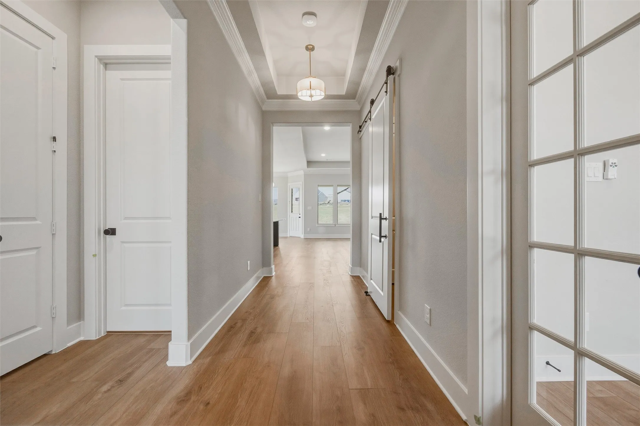 Hallway featuring wood-finish flooring, a tray ceiling with pendant lighting, a barn door, and French doors