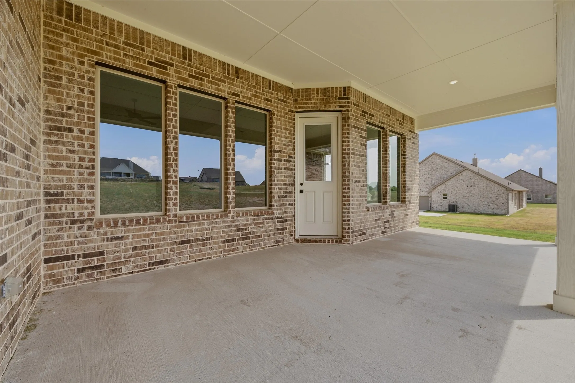 Covered concrete patio with brick exterior, multiple windows, and a white door with glass paneling