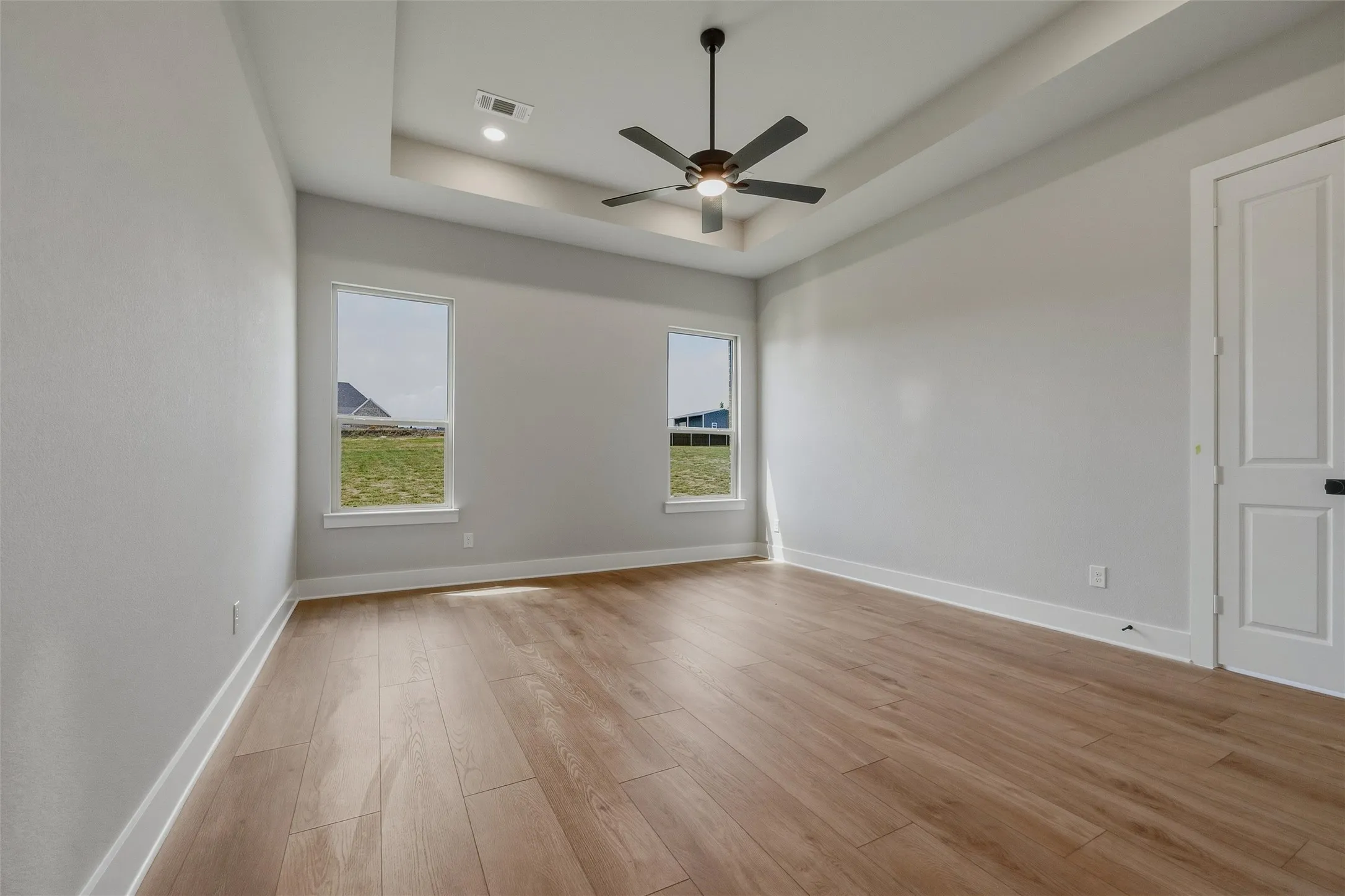 Wood-finish flooring with white trim, tray ceiling with recessed lighting, and a ceiling fan