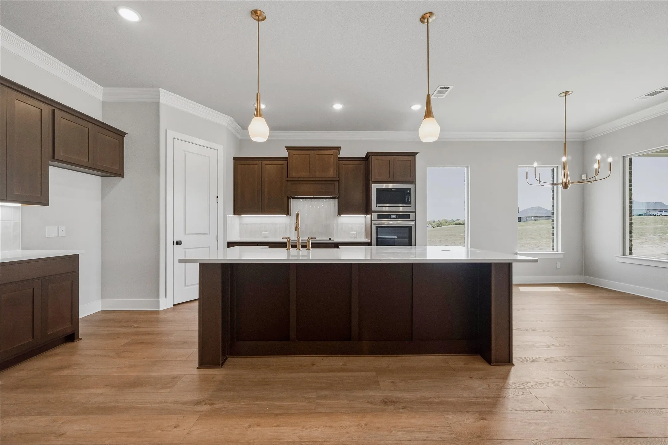 Open-concept kitchen featuring an oversized island with white countertop, dark wood-finish cabinetry, stainless steel appliances, and wood-finish flooring