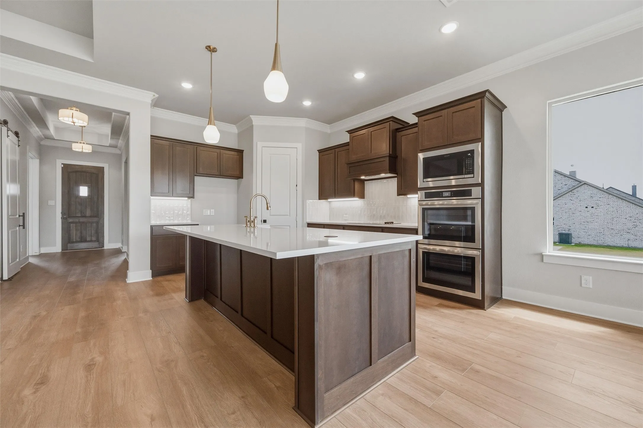 Gourmet kitchen featuring a large central island with white countertop, dark wood-finish cabinetry, stainless steel double ovens, and wood-finish flooring