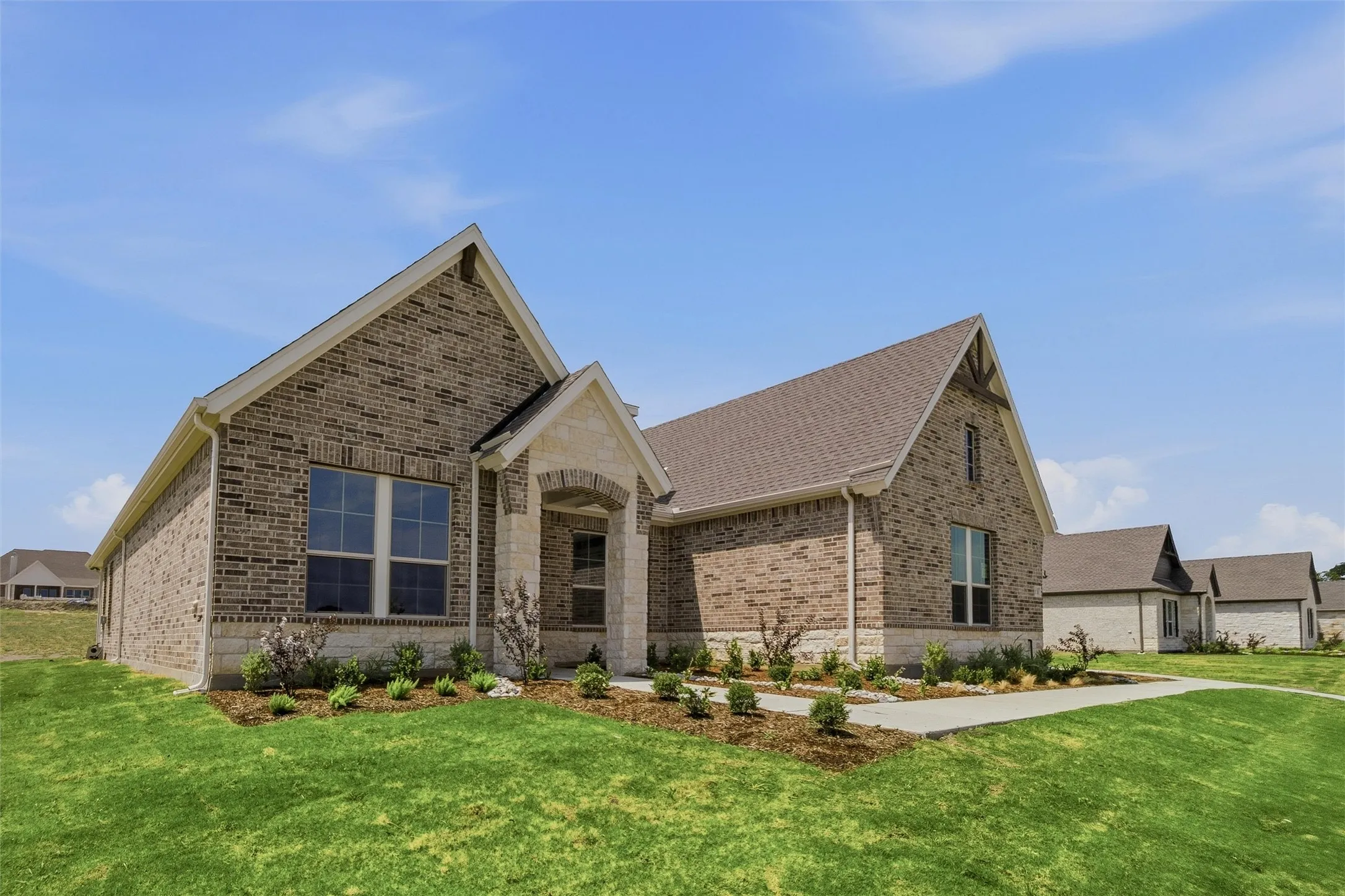 Brick and stone facade, gabled rooflines, covered entry, front landscaping, and concrete walkways