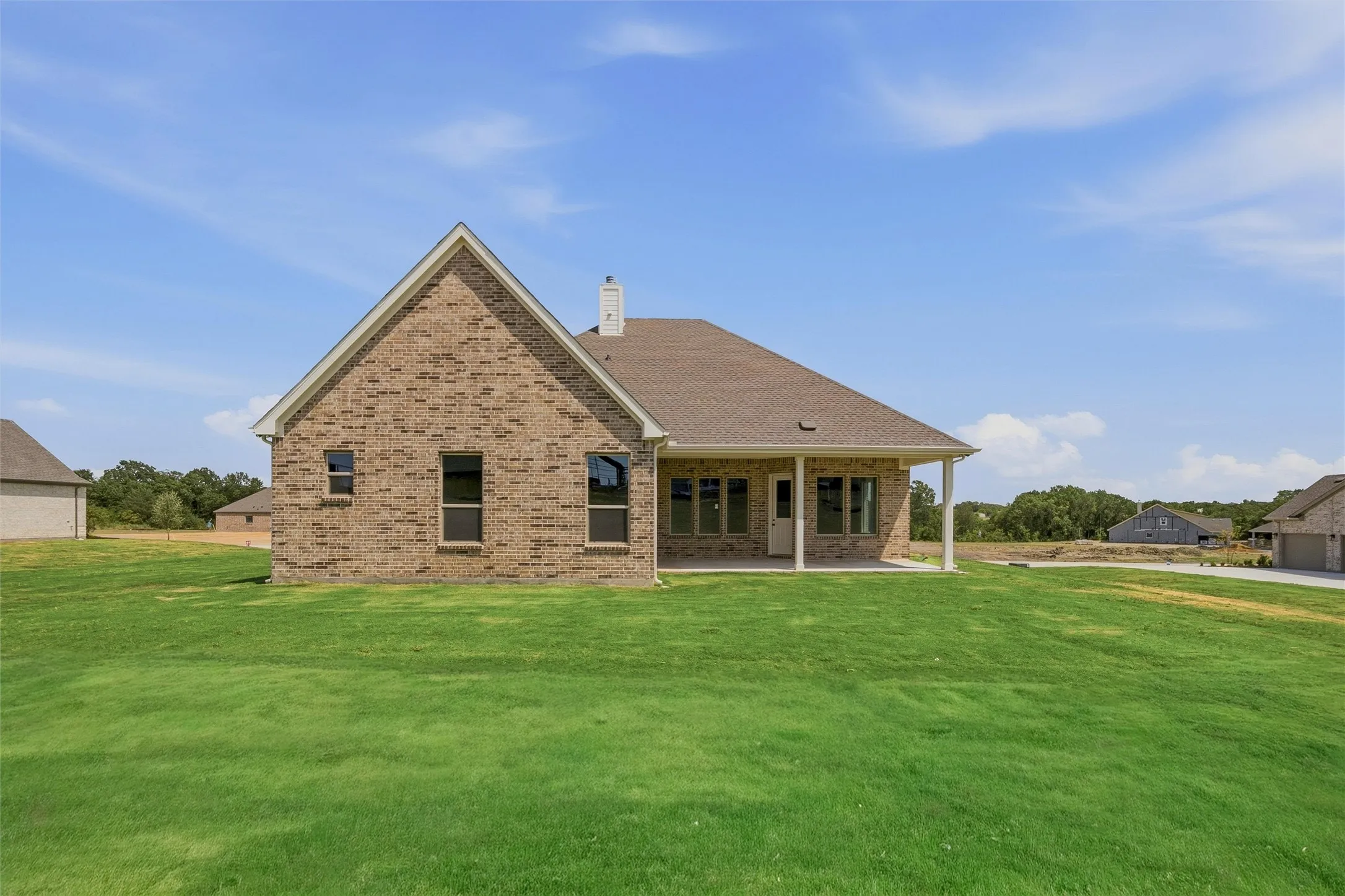 Expansive green lawn surrounds a brick exterior home with multiple windows and a covered patio