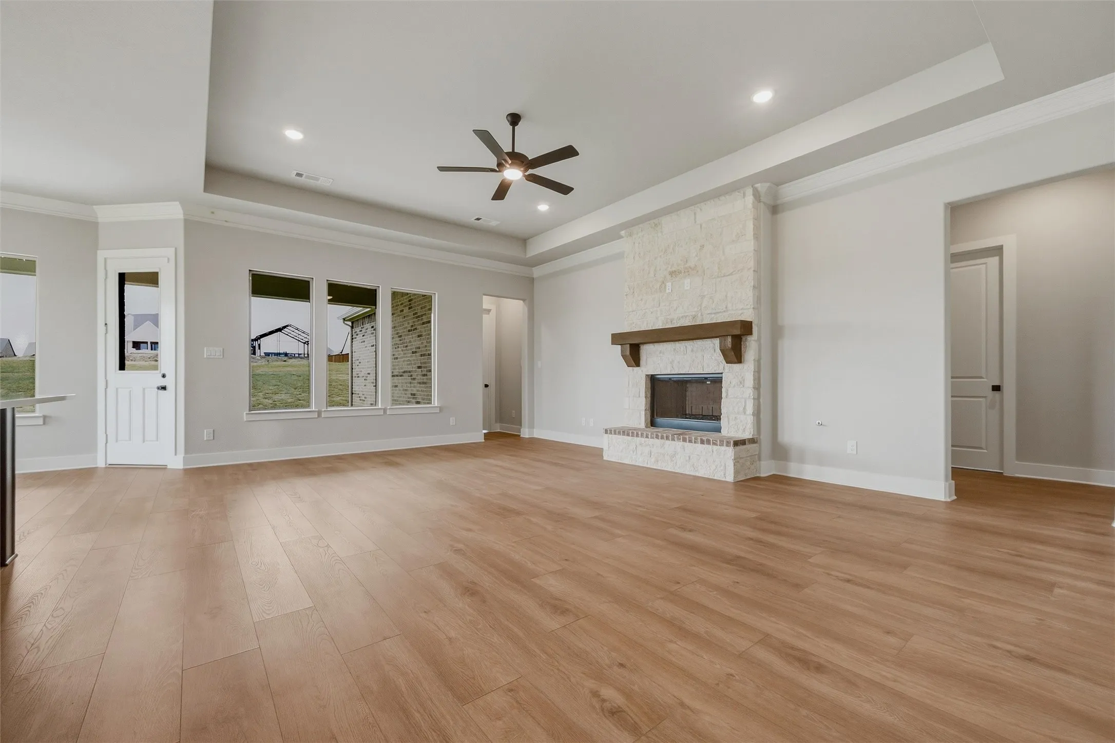 Open-concept living area featuring wood-finish flooring, a stone-clad fireplace with a wood mantle, and recessed ceiling lighting