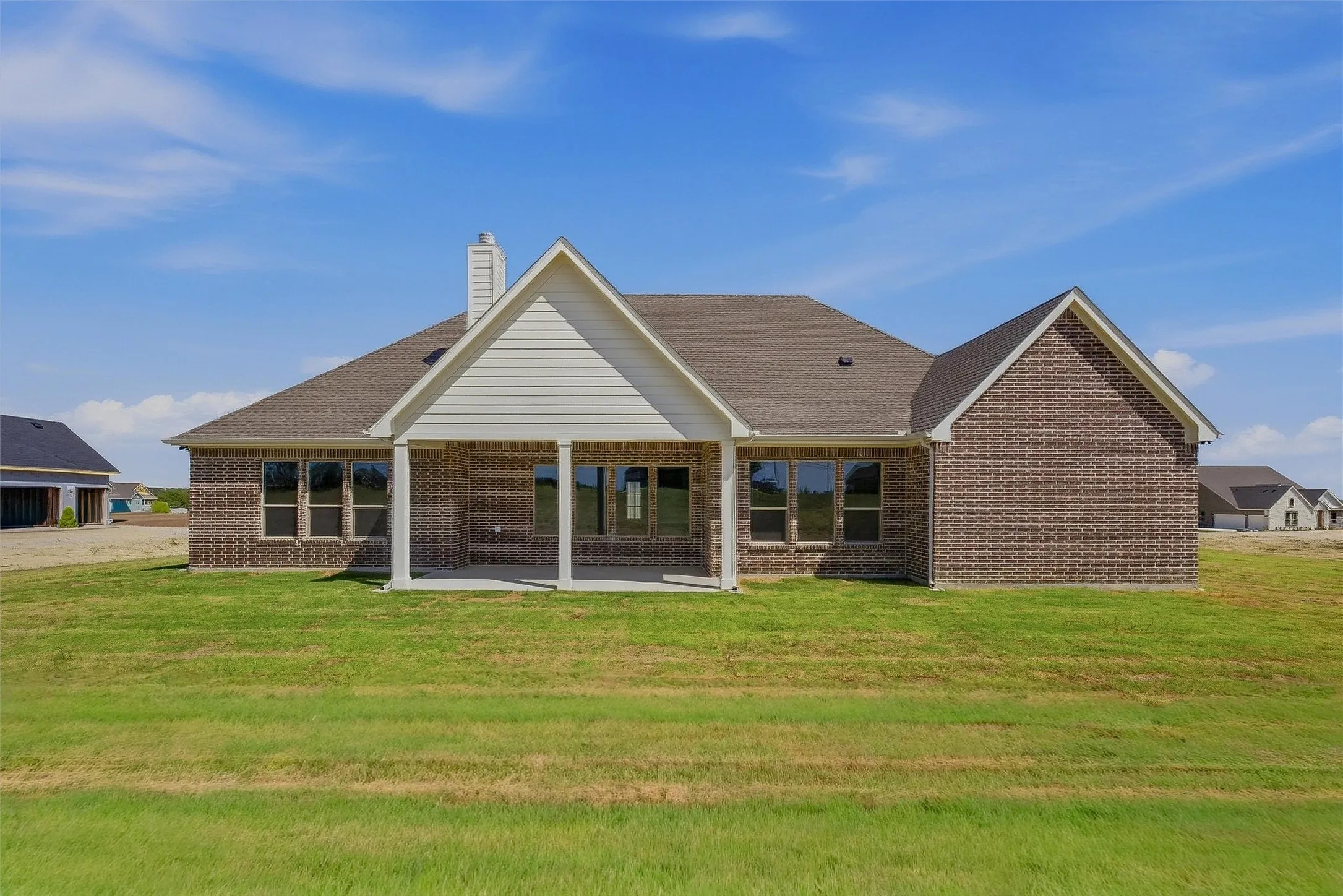 Brick exterior with a covered patio, multiple windows, and a shingled roof
