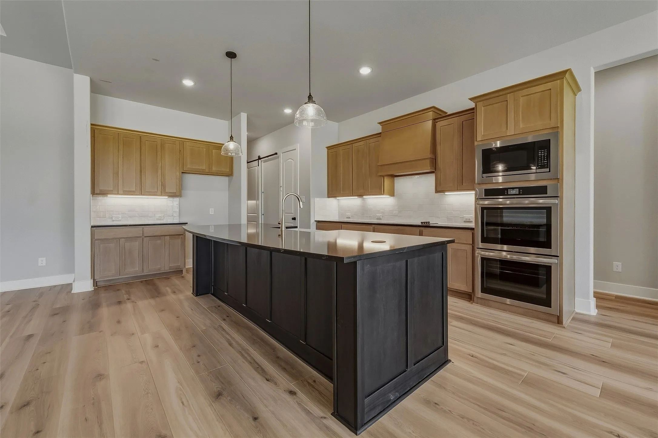 Wood-finish flooring throughout, featuring a dark-toned kitchen island with a built-in sink and two pendant lights