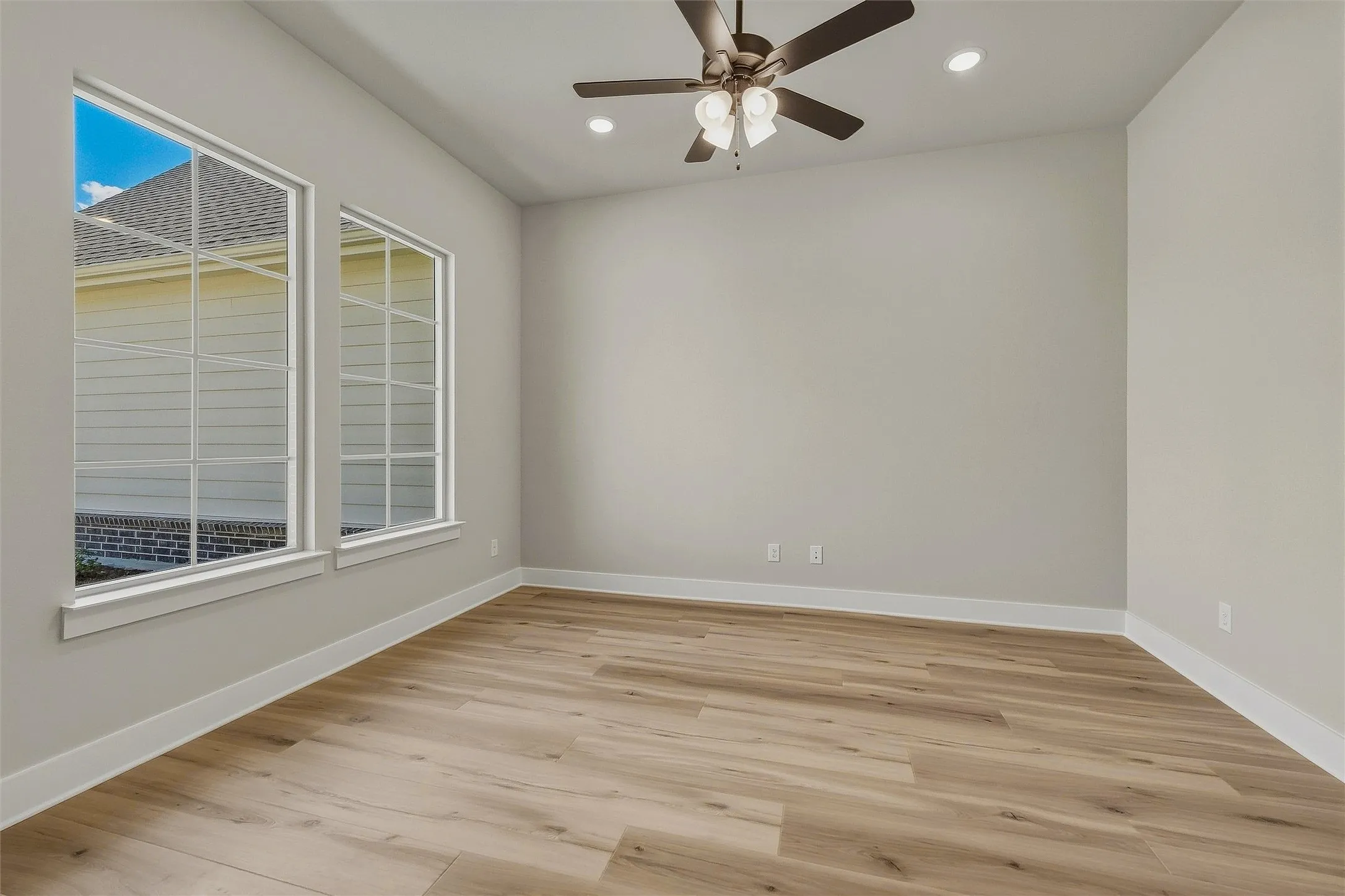 Wood-finish flooring, two large windows, recessed lighting, and a ceiling fan