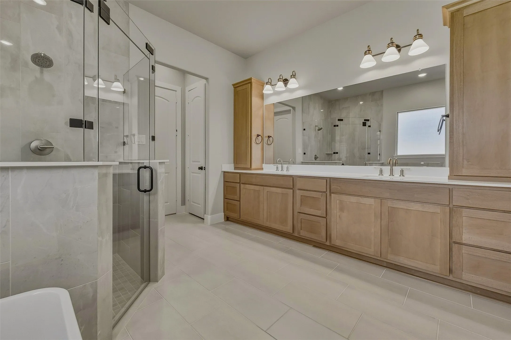 Spacious bathroom featuring a frameless glass shower enclosure, dual vanity with undermount sinks, wood-finish cabinetry, and wide-format tile​​‌​​​​‌​​‌‌​‌‌​​​‌‌​‌​‌​‌​​​‌​​ flooring