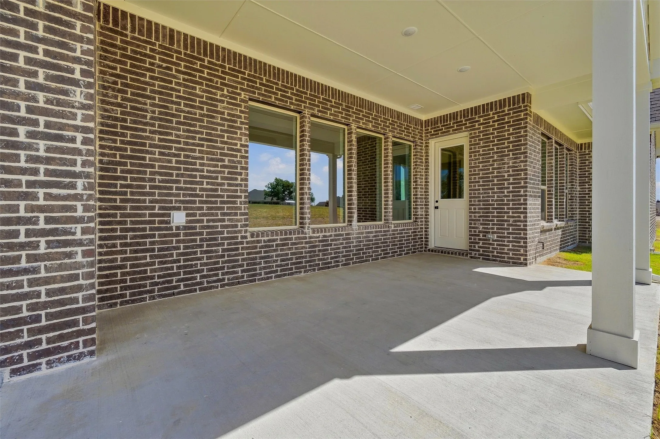 Covered patio featuring a solid concrete surface, brick exterior, multiple windows, recessed lighting, and a glass-paneled door