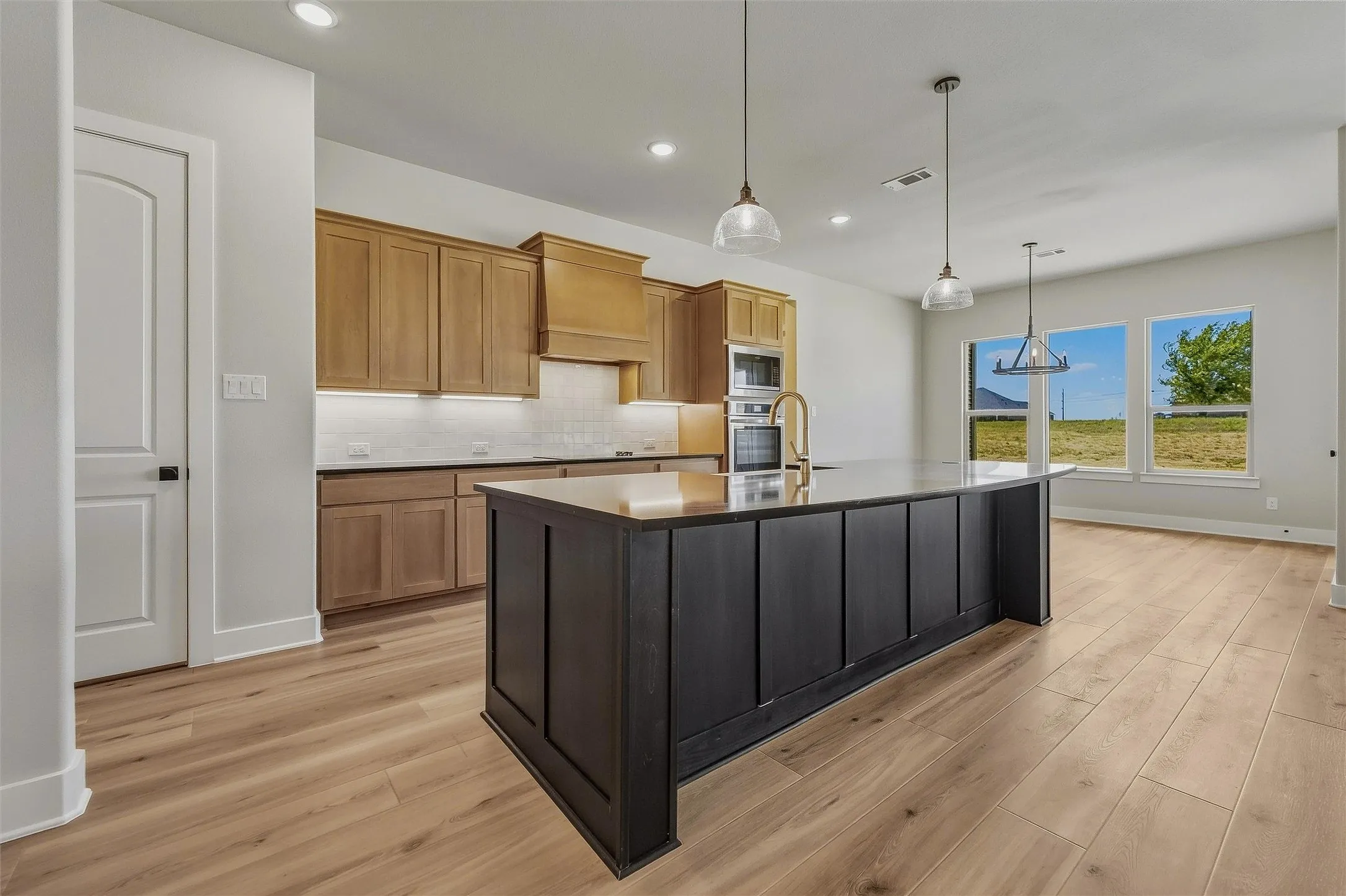 Open-concept kitchen with wood-finish flooring, recessed lighting, and a spacious island with pendant lighting