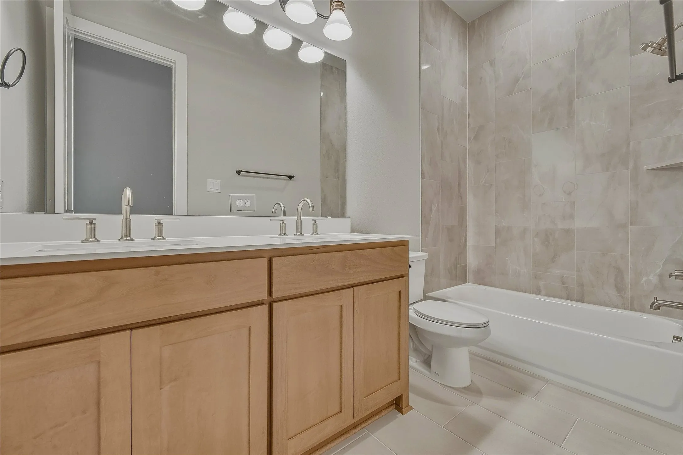 Dual sink vanity with light wood-finish cabinetry, a large mirror, and contemporary lighting