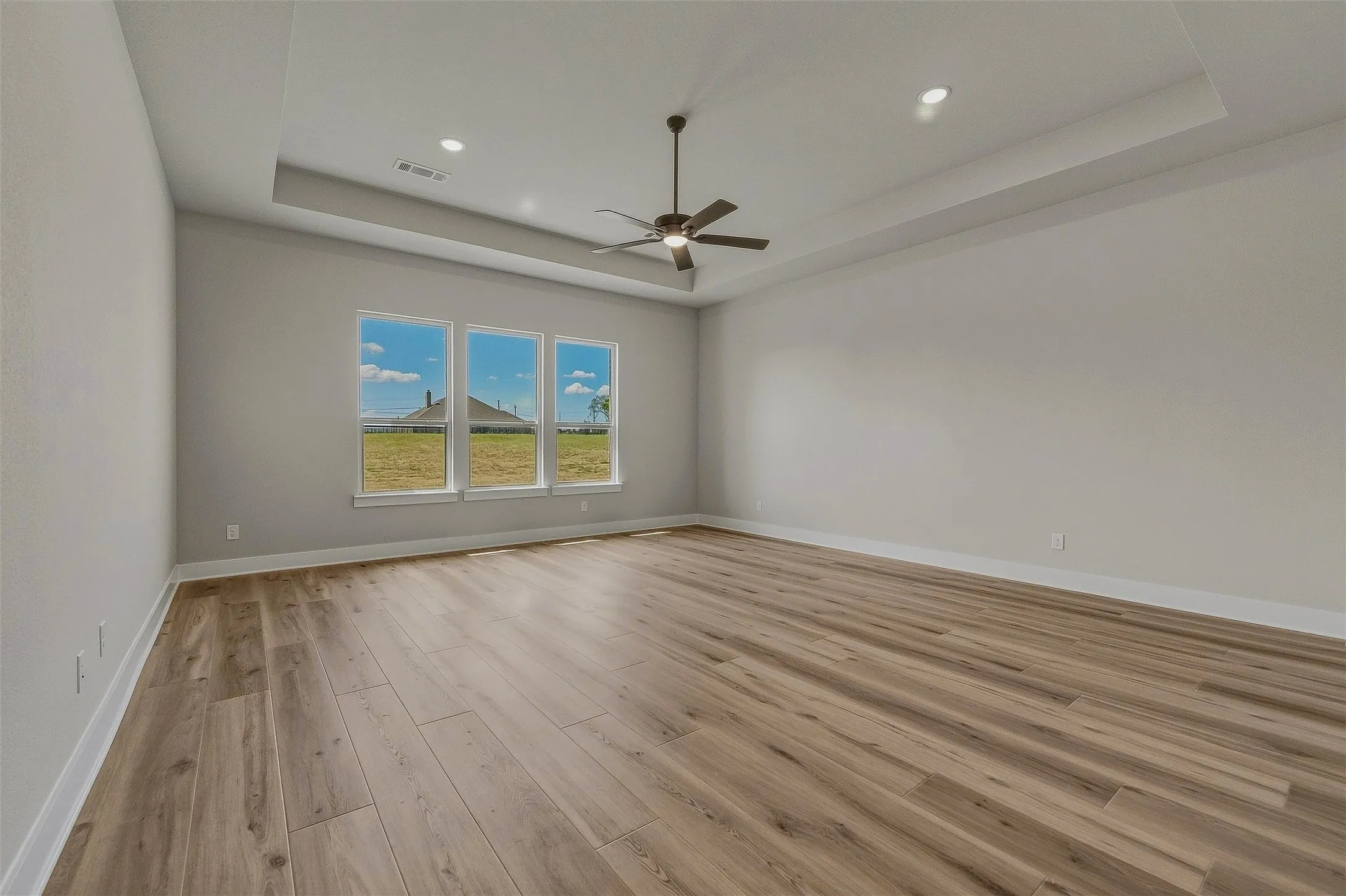 Tray ceiling with recessed lighting and a ceiling fan, wood-finish flooring, and three large windows