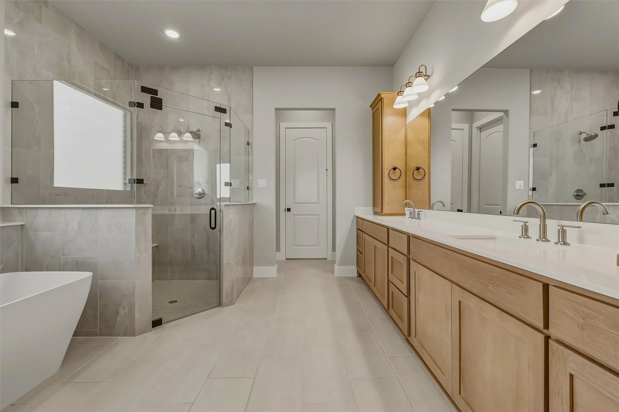 Dual sink vanity with light wood cabinetry, stone countertops, and a full-width mirror