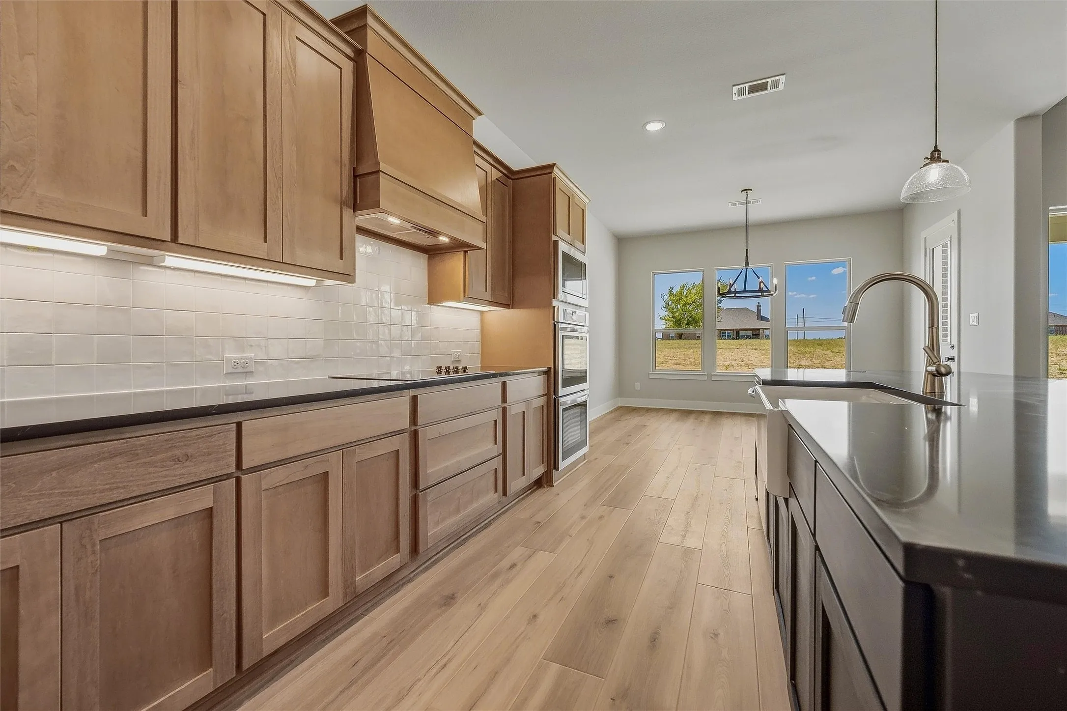Kitchen featuring wood-finish cabinetry, subway tile backsplash, built-in double oven, and a large island with an integrated sink
