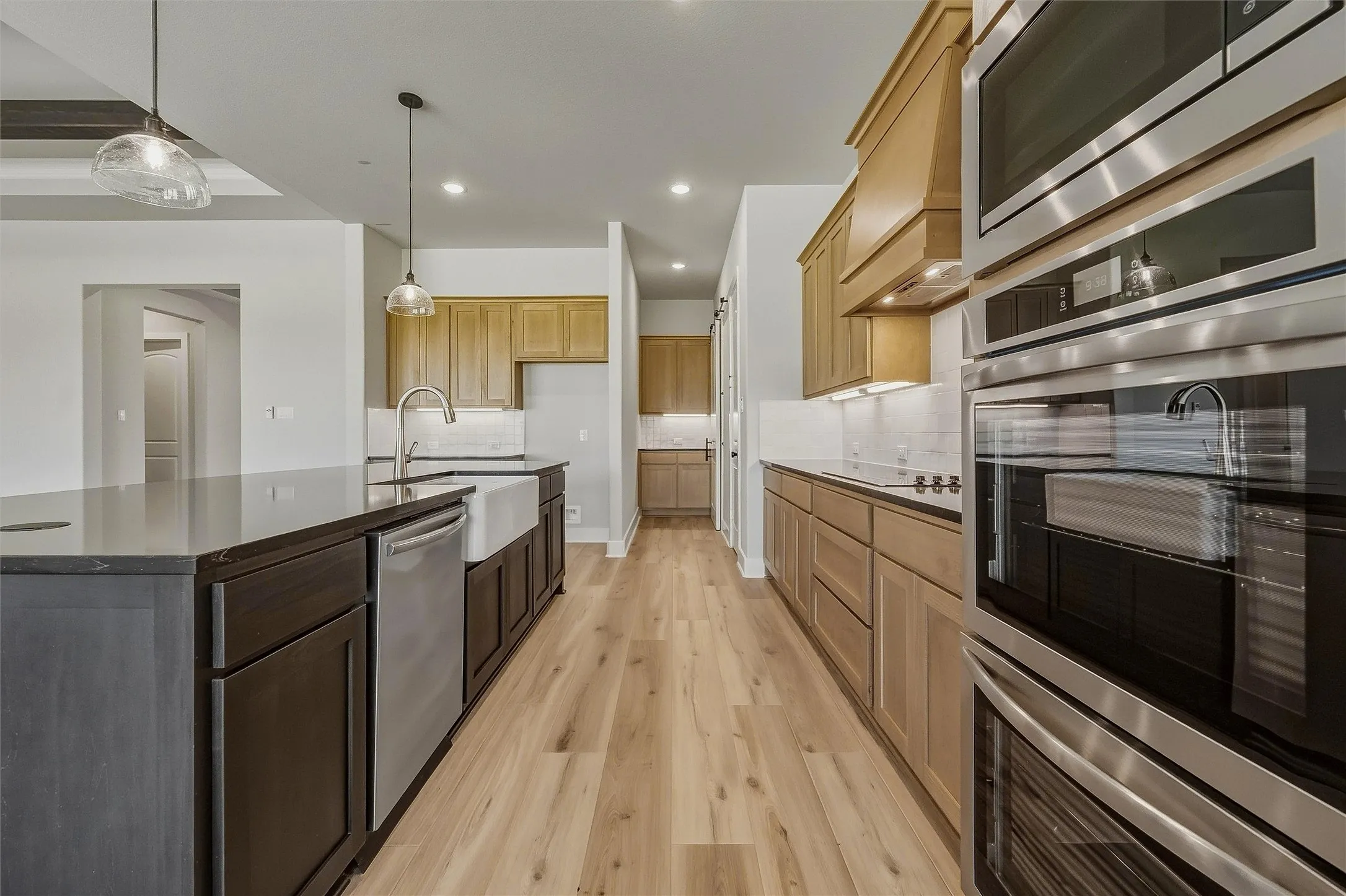 Kitchen featuring wood-finish flooring, stainless steel appliances, a large center island with a stone countertop, a farmhouse sink, and light wood cabinetry
