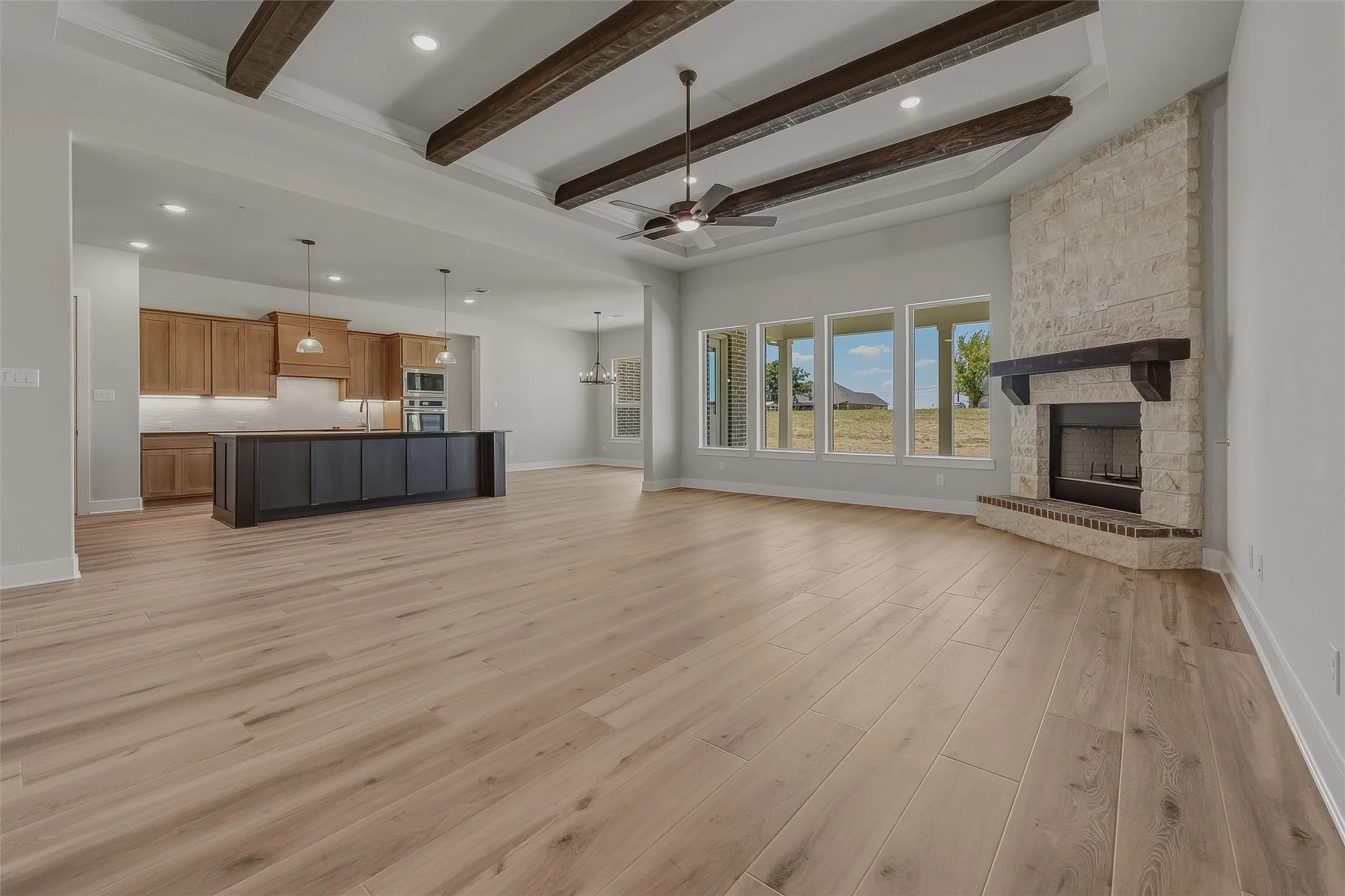 Open-concept living area featuring wood-finish flooring, a stone-clad fireplace with a dark wood mantel, and multiple windows