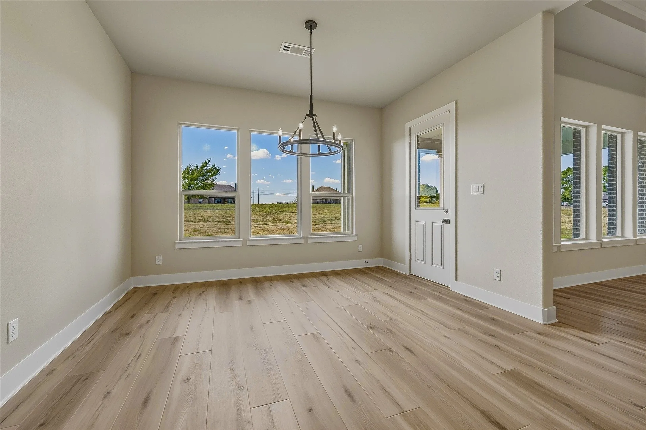 Spacious room featuring multiple windows, wood-finish flooring, a contemporary chandelier, and a paneled door with an integrated window